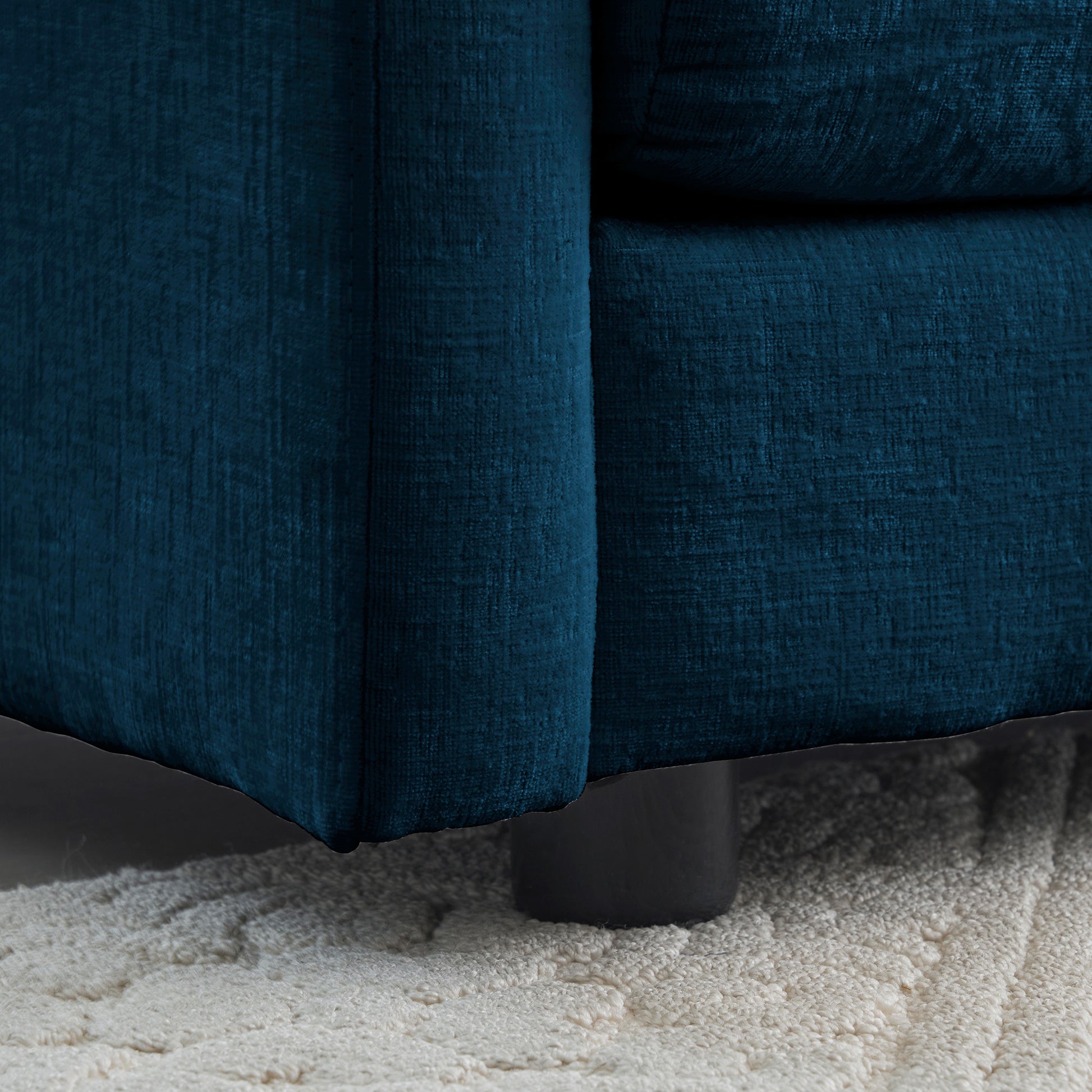 Closeup of teal textured fabric sofa detail with dark legs on a cream rug