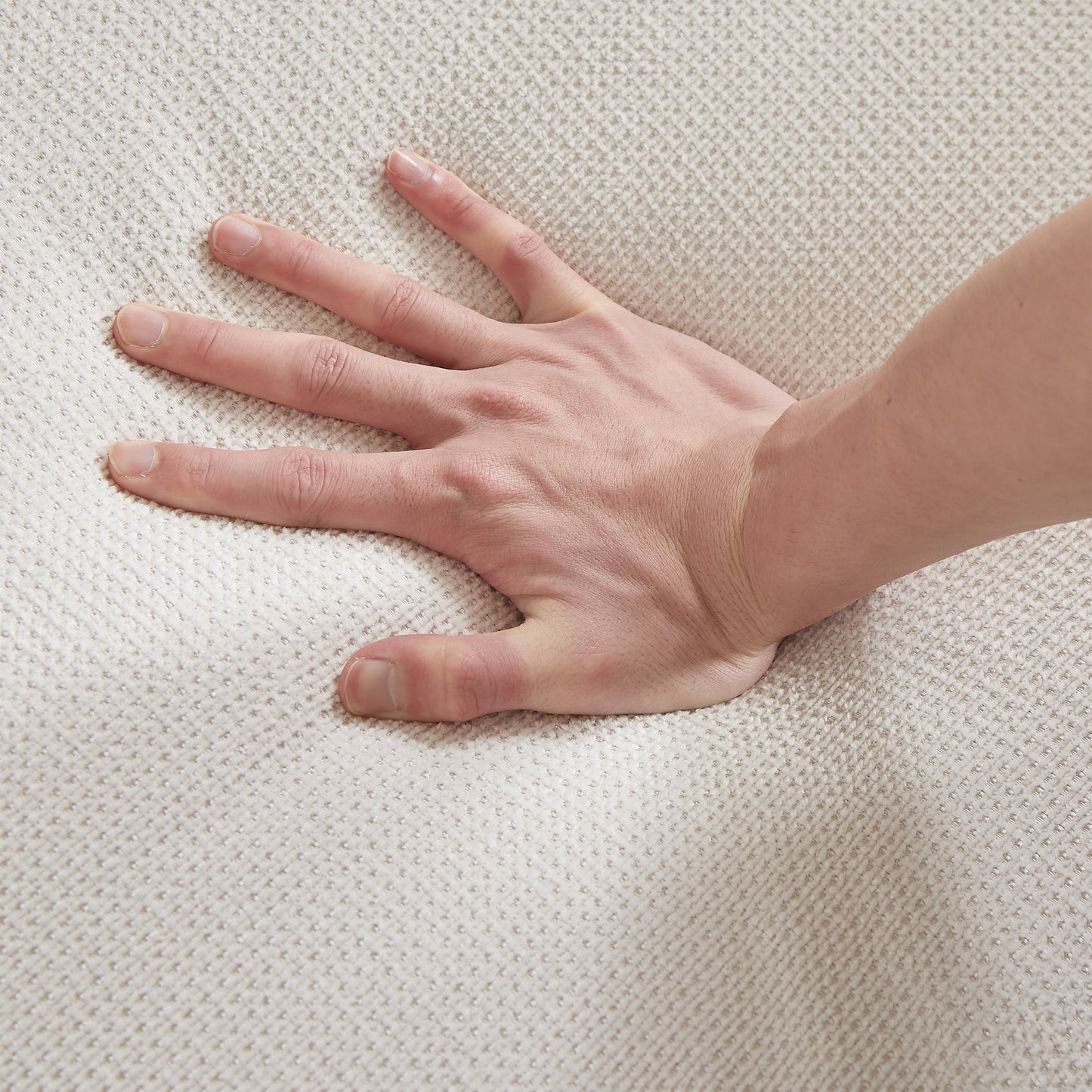 Hand pressing into soft textured beige upholstery fabric highlighting comfort