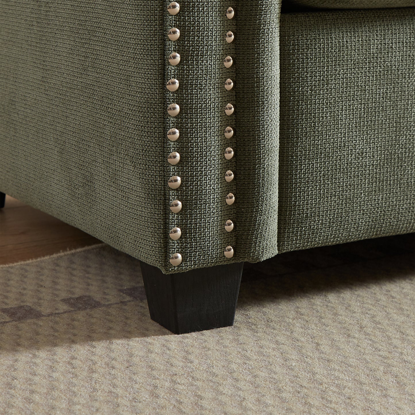 Green fabric sofa armrest with polished stud trim detail and dark wood leg