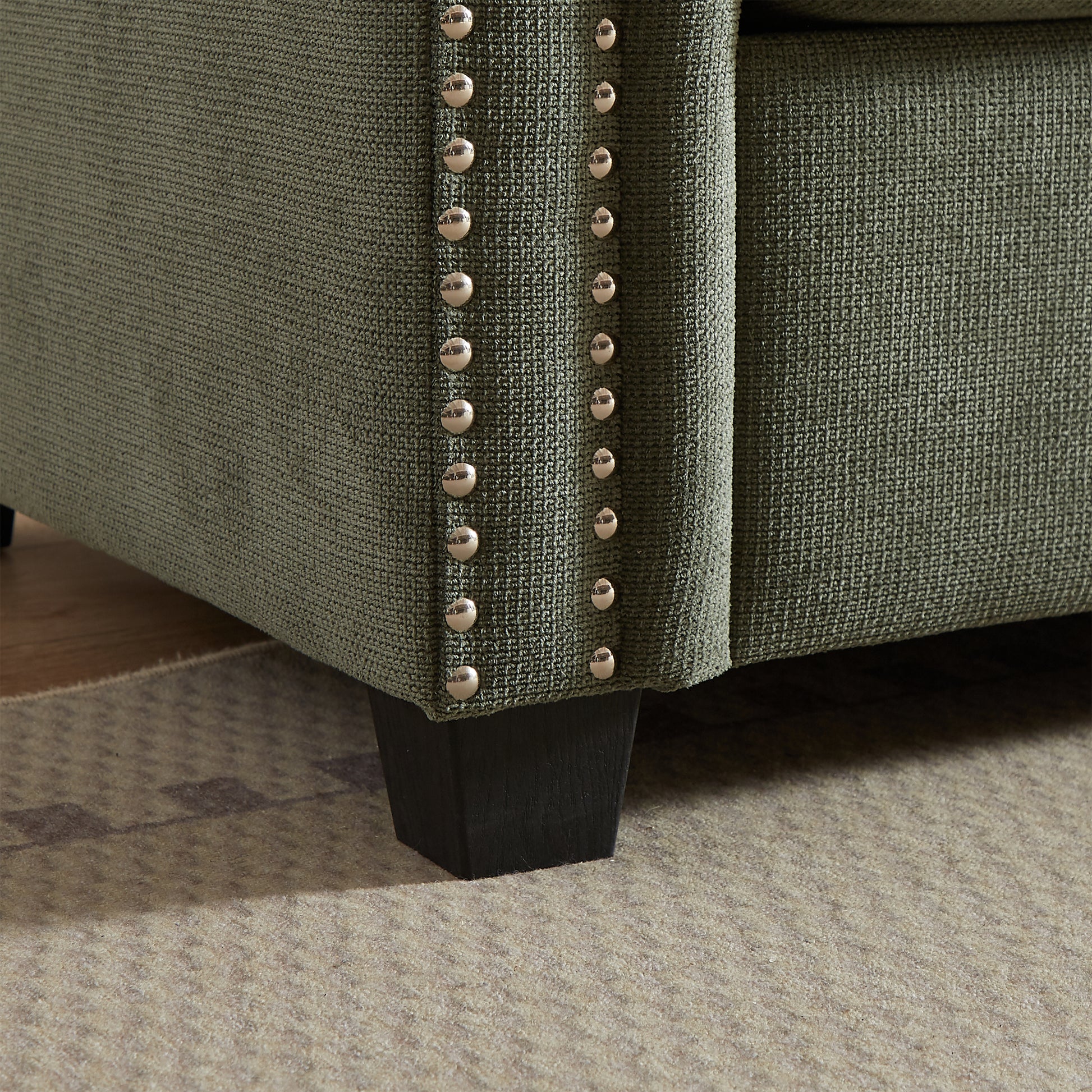 Green fabric sofa armrest with polished stud trim detail and dark wood leg