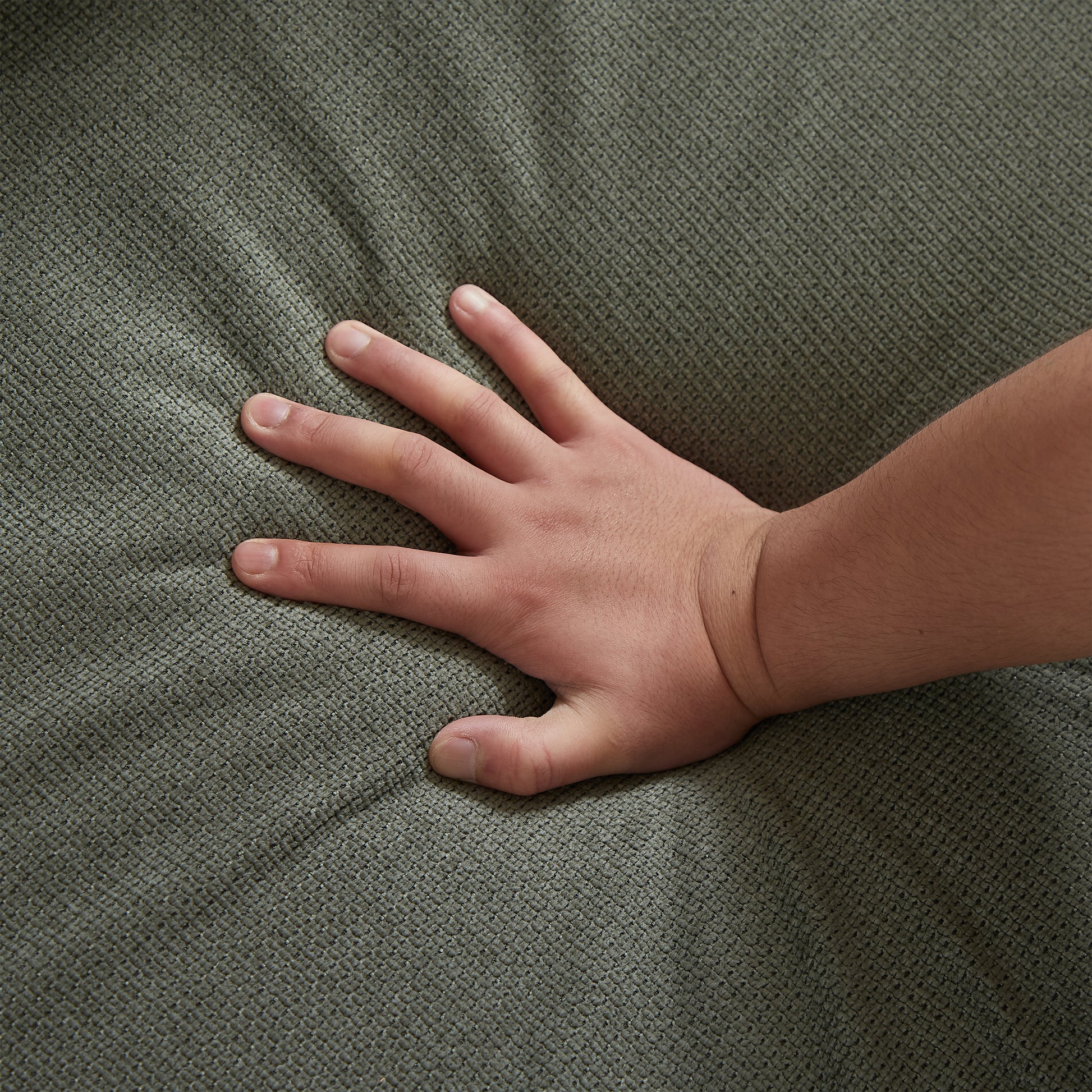 Closeup of a hand pressing into soft textured green upholstery fabric