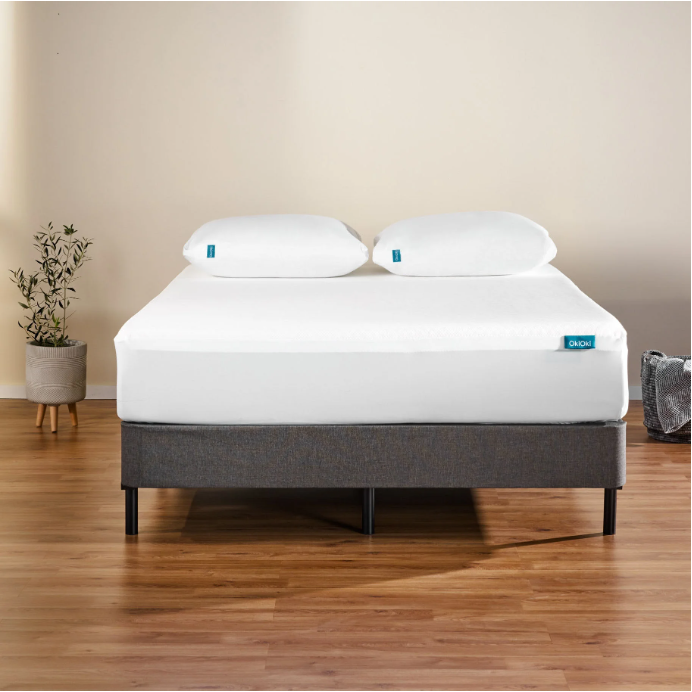 White memory foam mattress on a dark grey upholstered bed frame with two white pillows
