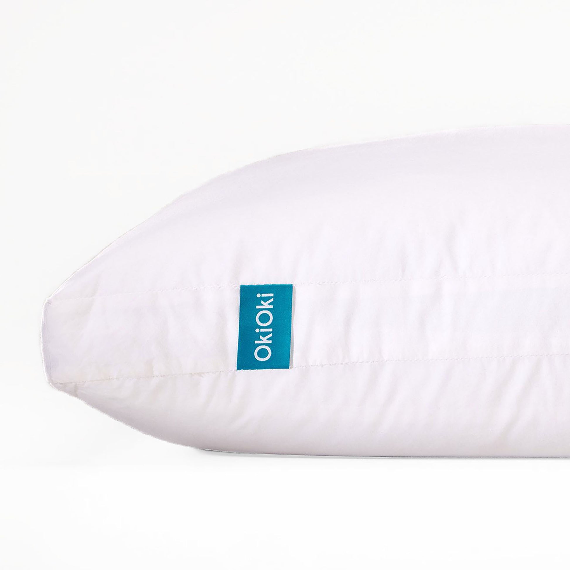 A soft white OkiOki pillow with a turquoise tag offering comfortable support for your head