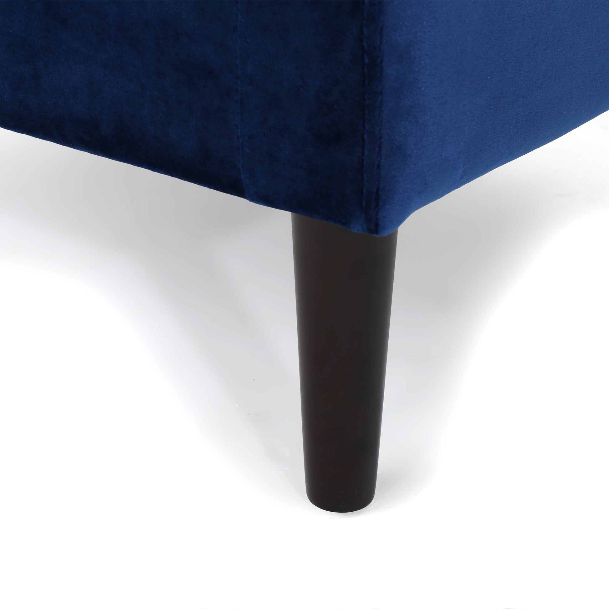 Closeup of a navy blue velvet sofa corner with a dark wooden tapered leg