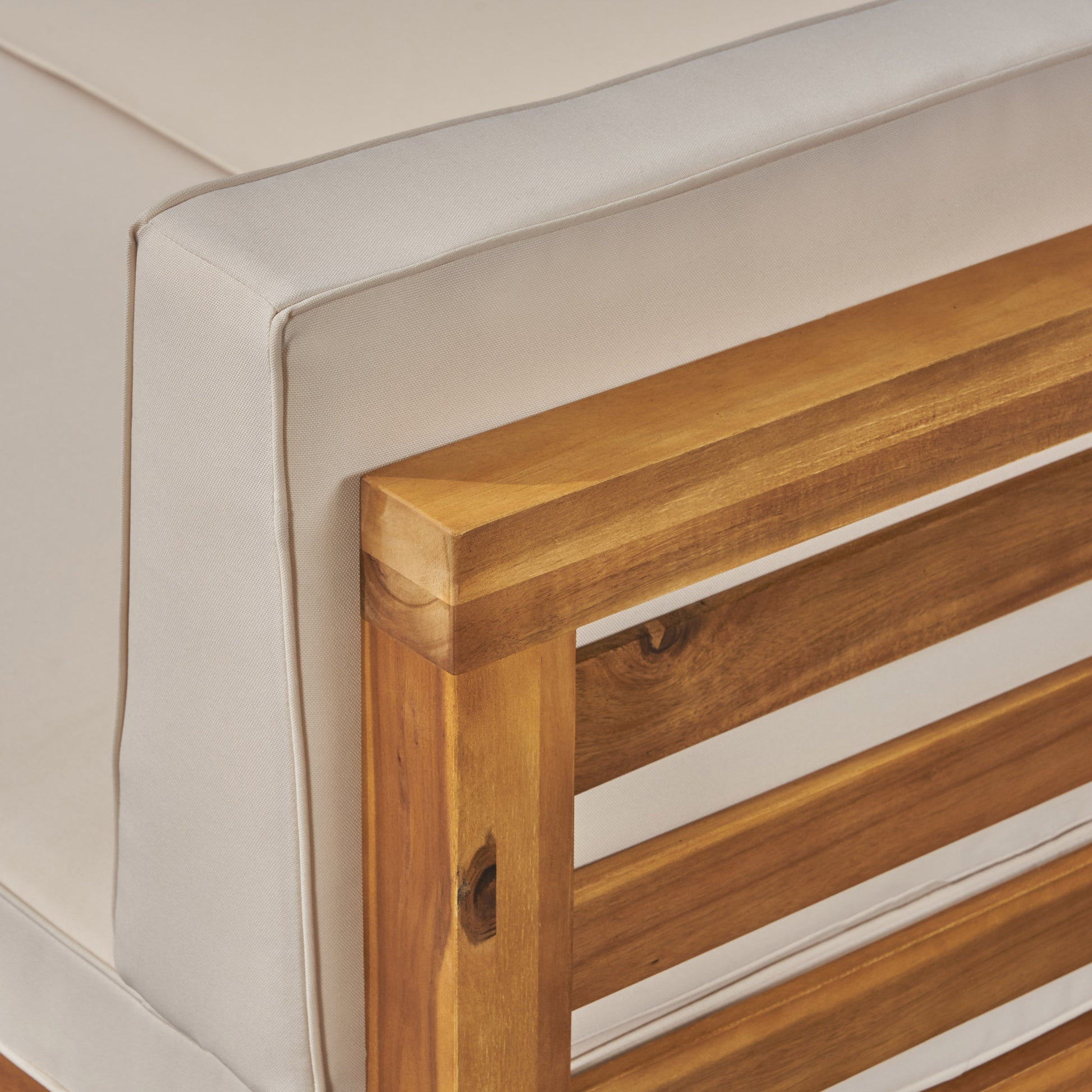 Closeup of beige outdoor patio sofa cushion with natural wood armrest detail