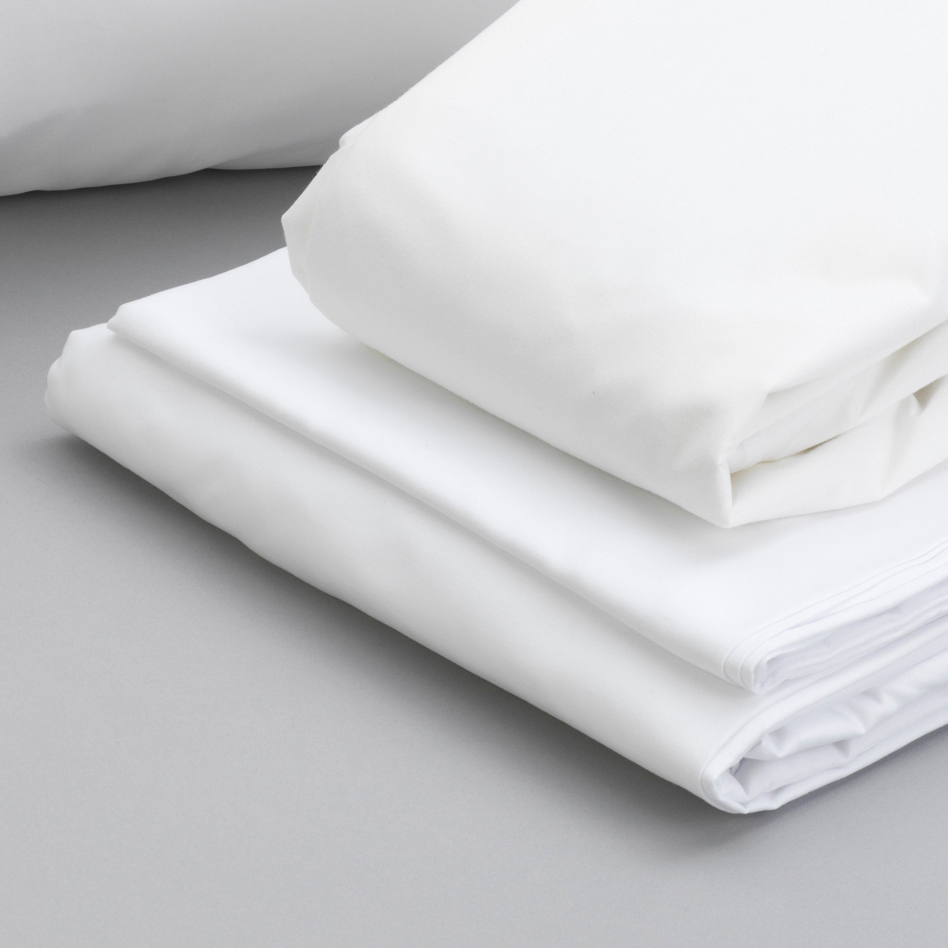 Crisp white cotton sheets folded neatly on a gray surface