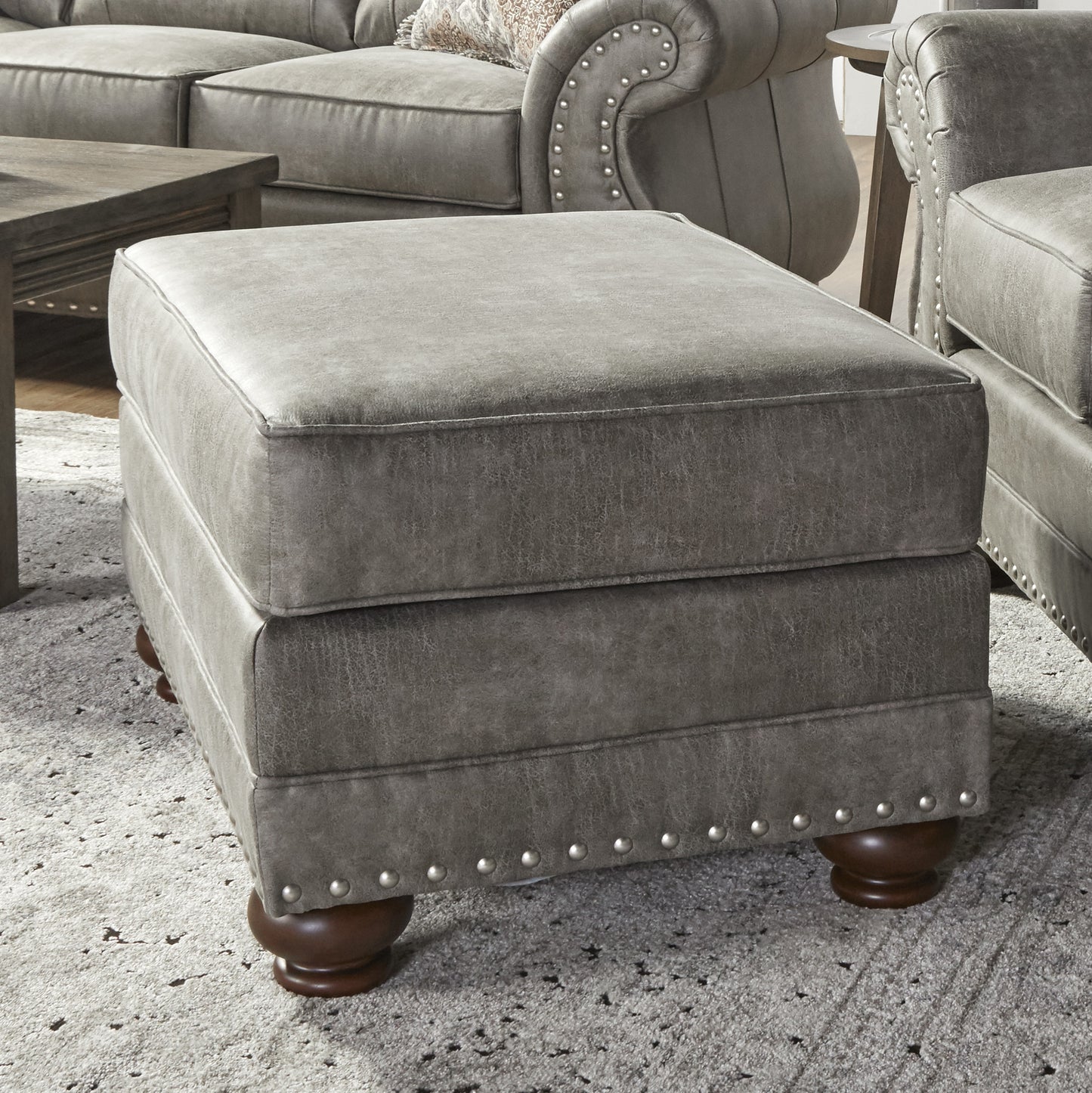 Square grey faux leather ottoman with decorative nailhead trim and turned wooden legs