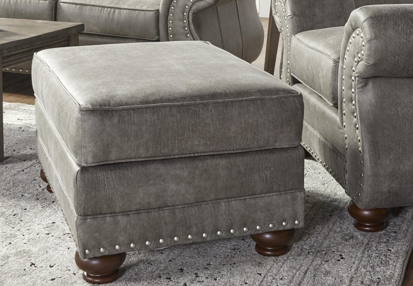 Gray upholstered ottoman with silver nailhead trim and dark wooden legs
