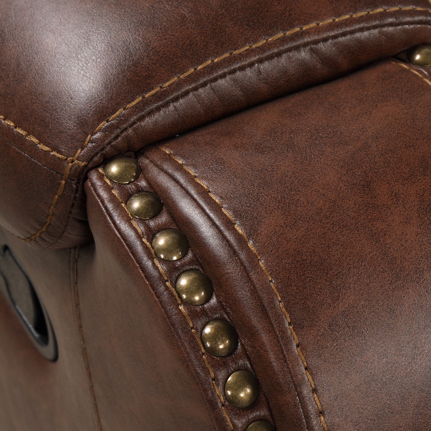 Brown leather armchair detail with brass nailhead trim and stitching
