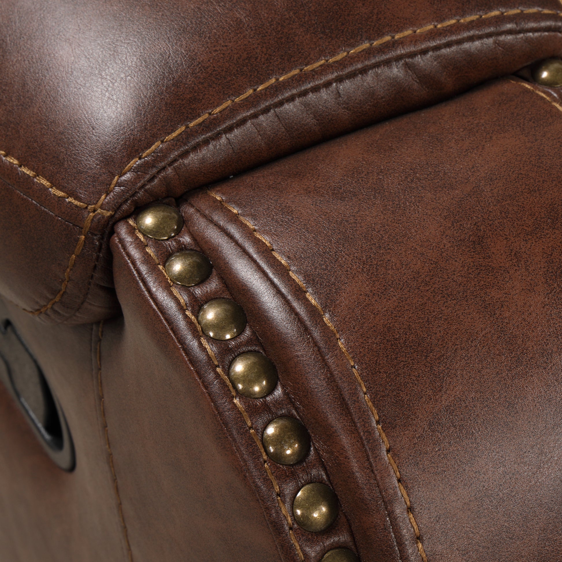 Detail of distressed brown faux leather recliner with brass nailhead trim and stitching