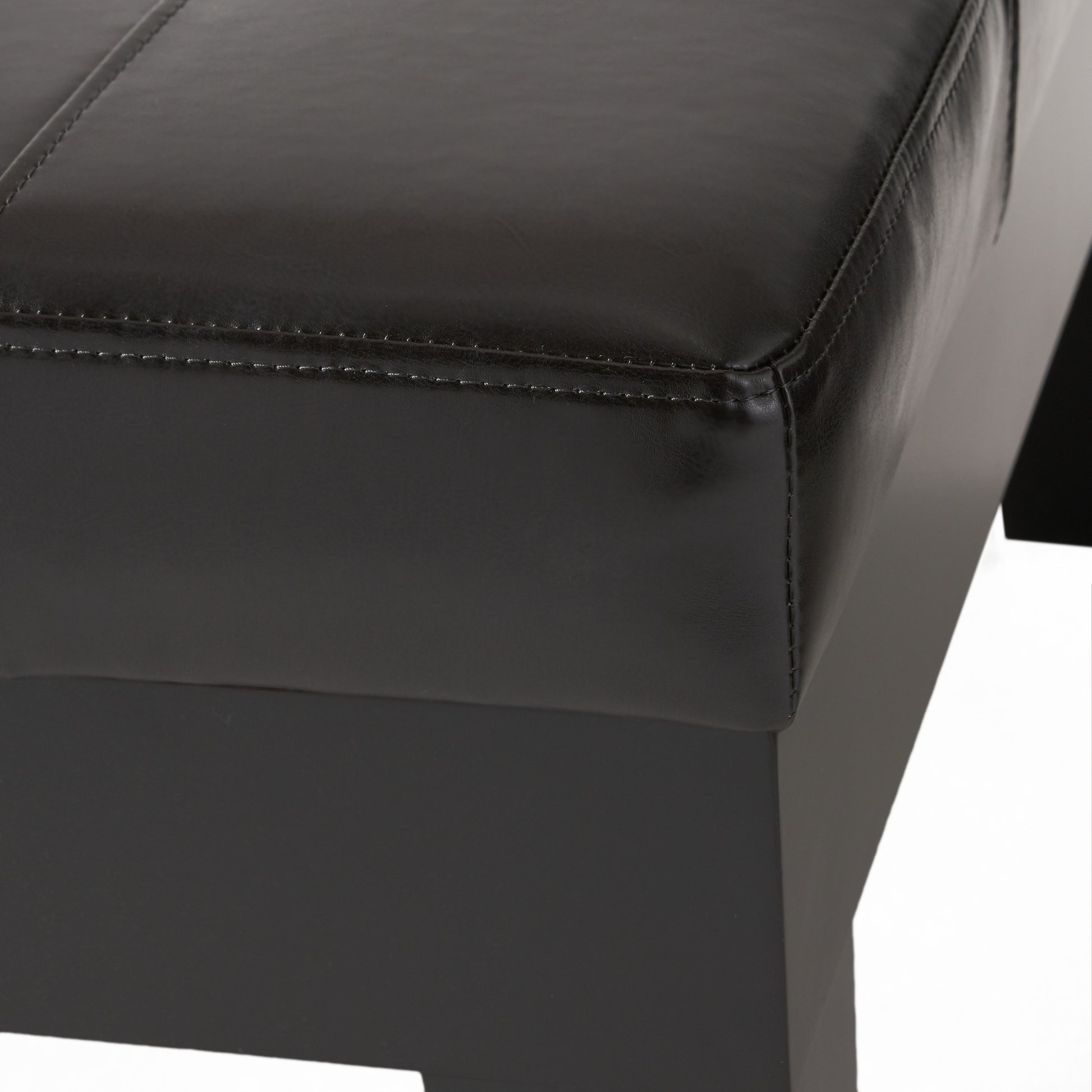Closeup of a black faux leather ottoman with stitched detailing on the top surface