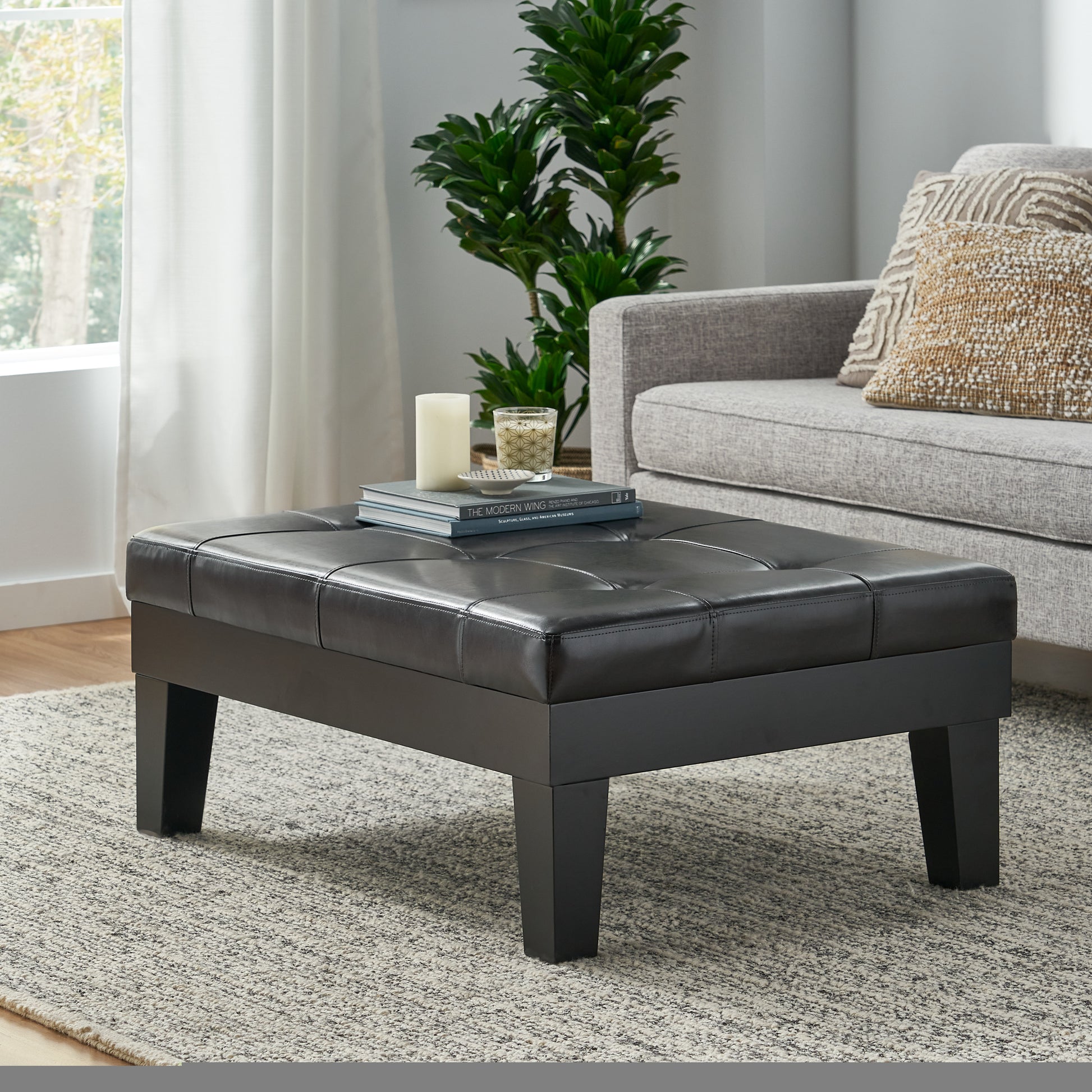 Black tufted leather ottoman with square wooden legs styled as a coffee table
