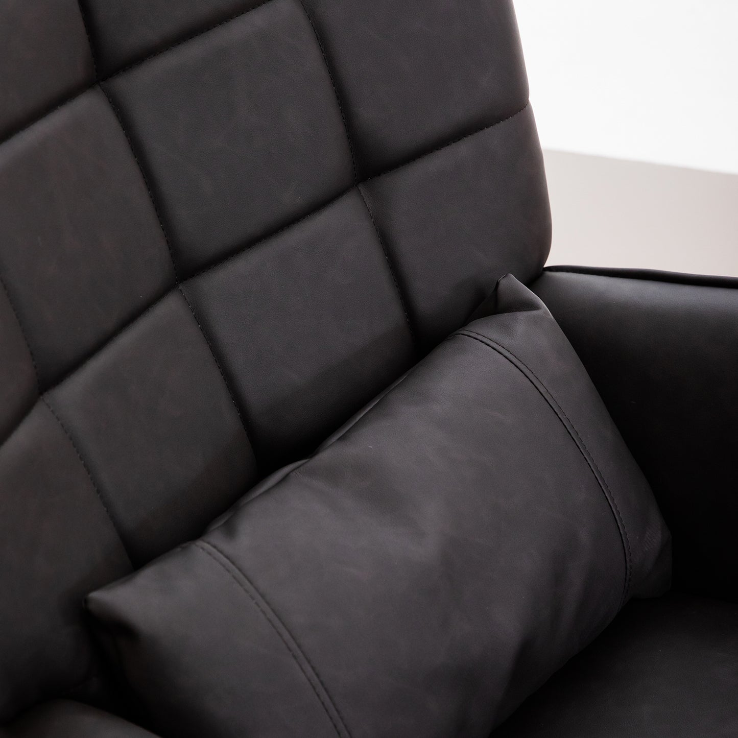 Closeup of a black leather chair with diamond tufting and a matching throw pillow
