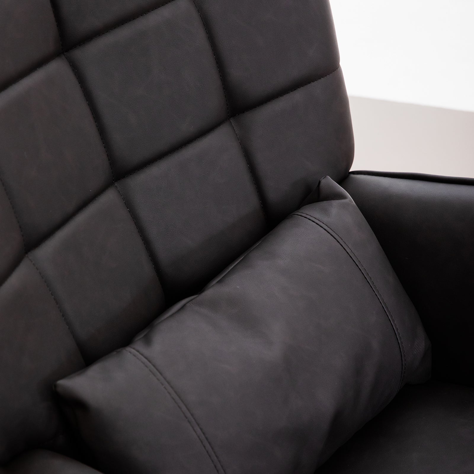 Closeup of a black leather chair with diamond tufting and a matching throw pillow