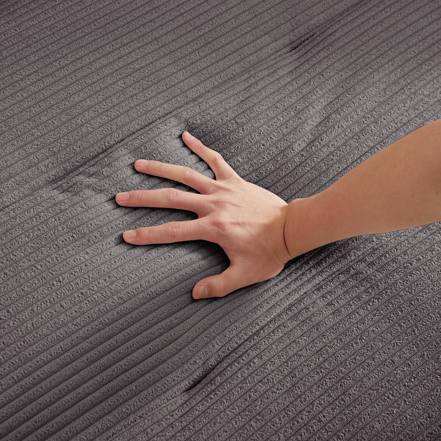 Closeup of a hand pressing into plush charcoal grey corduroy fabric