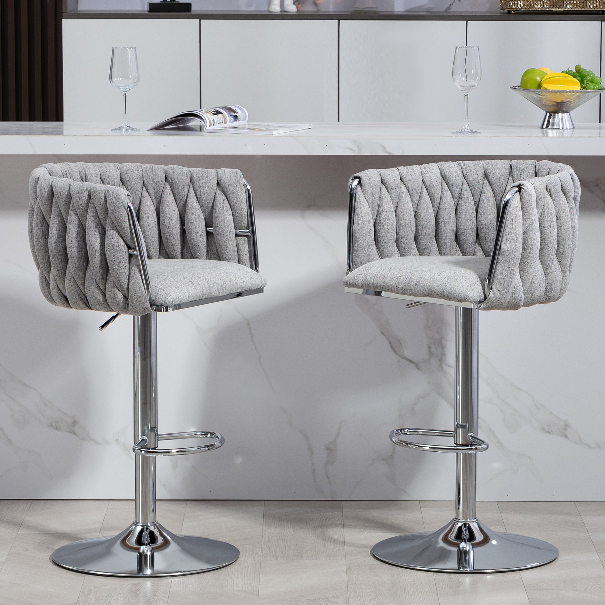 Two upholstered grey bar stools with chrome bases and adjustable height feature tufted backs
