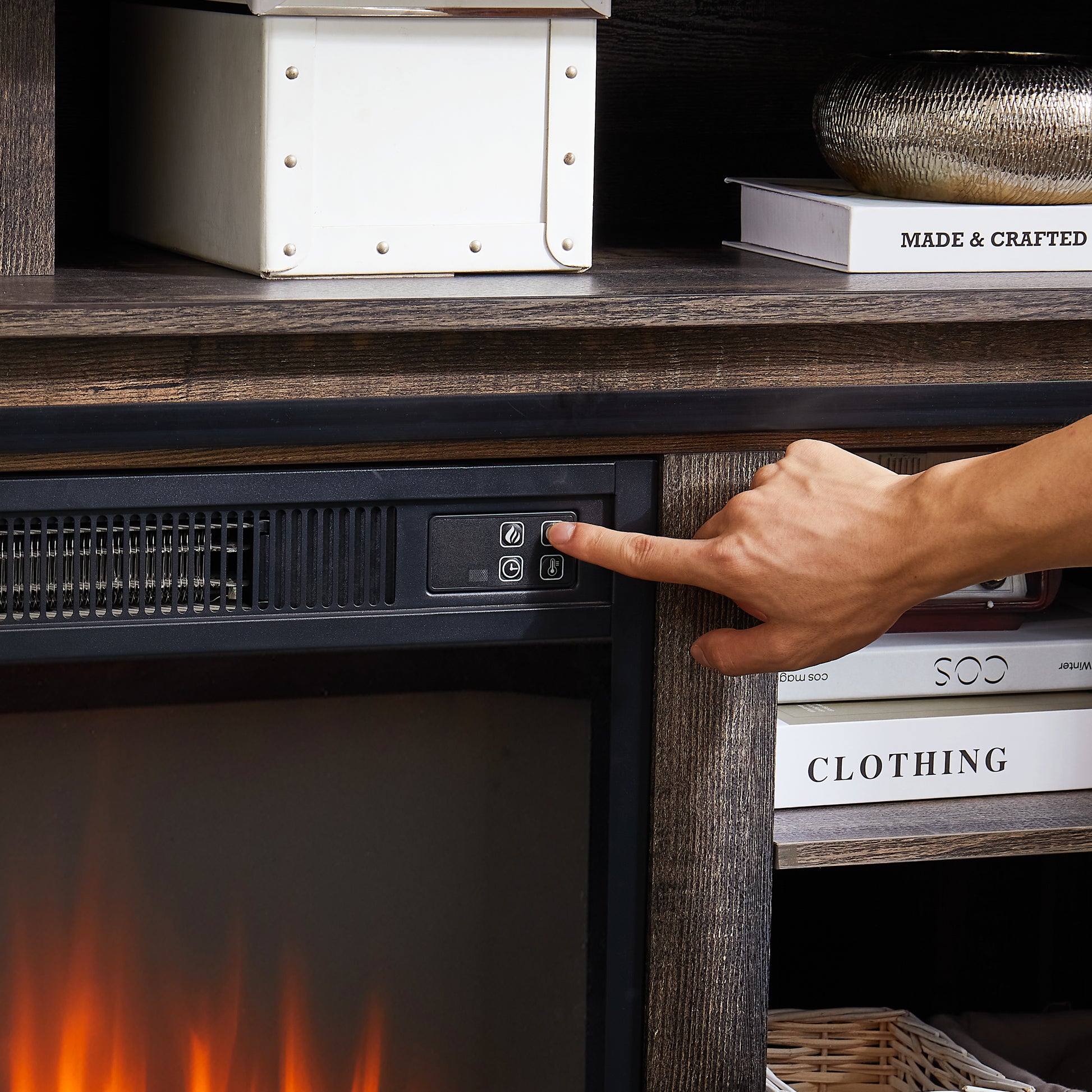 Closeup of a hand pressing the control button on a black electric fireplace unit with a flame icon