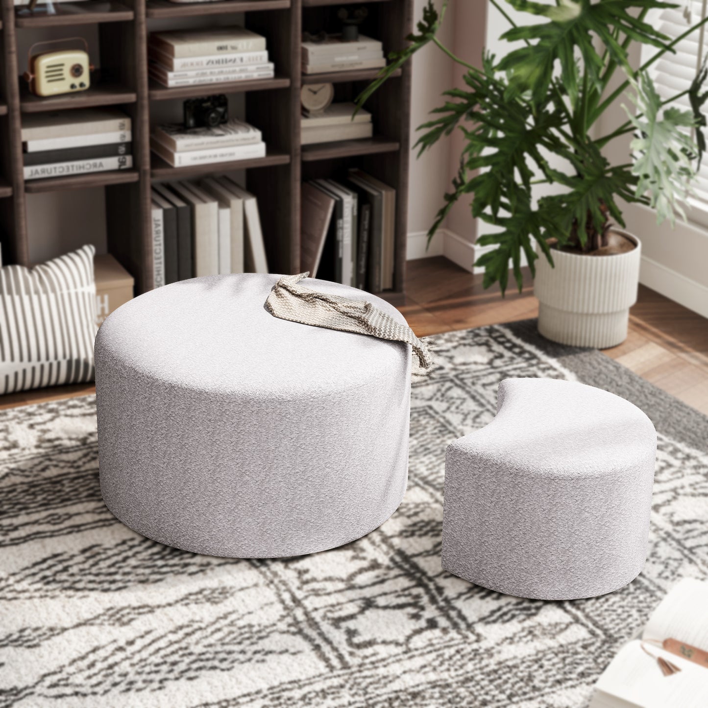 Round light gray boucle ottoman with a throw blanket draped over it