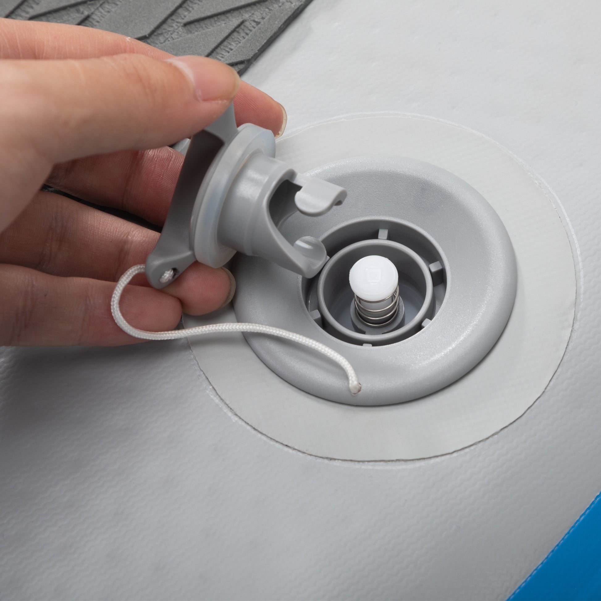 Gray inflatable boat valve with a white stopper being secured by a hand