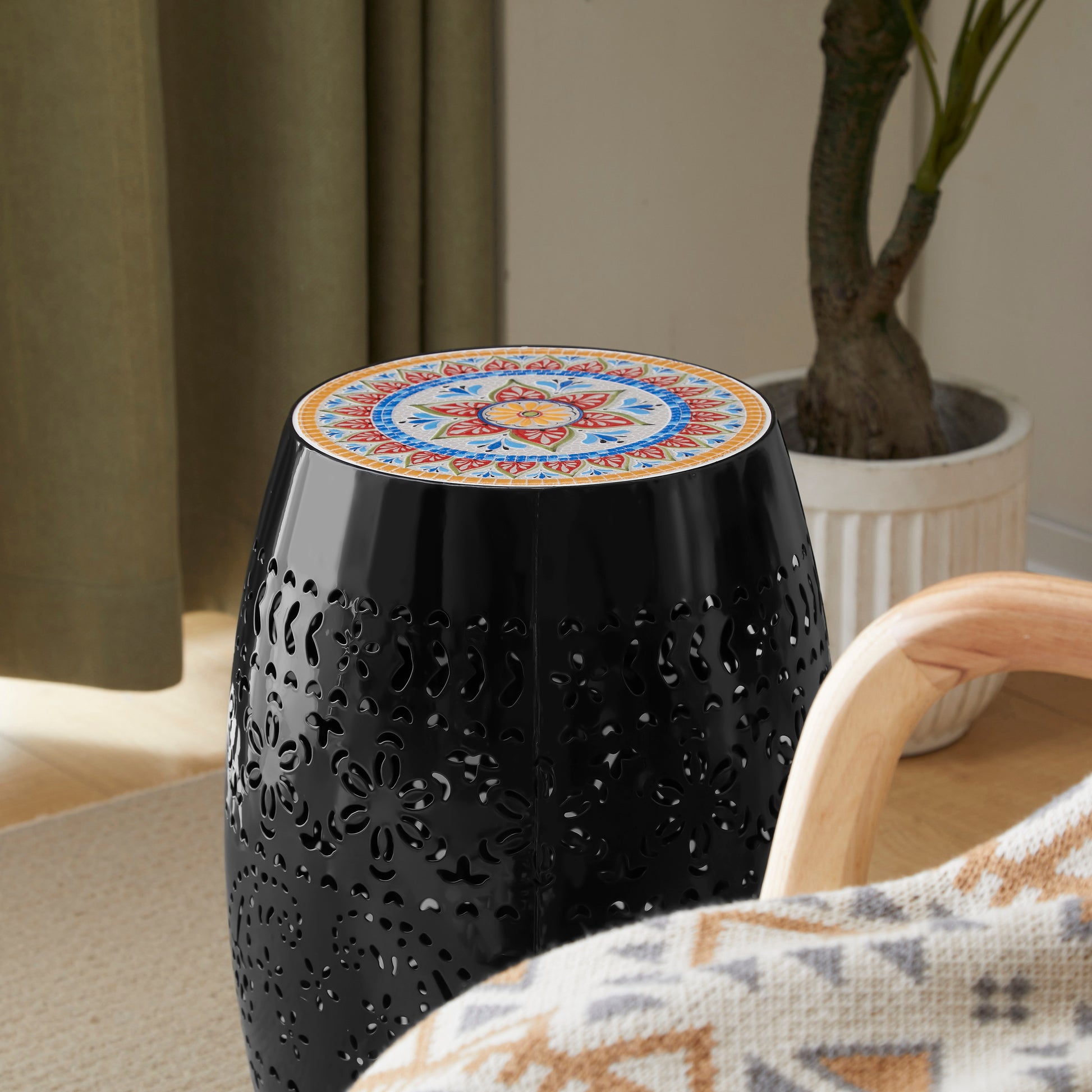 Black metal garden stool with ornate cutouts and a colorful mosaic tile top