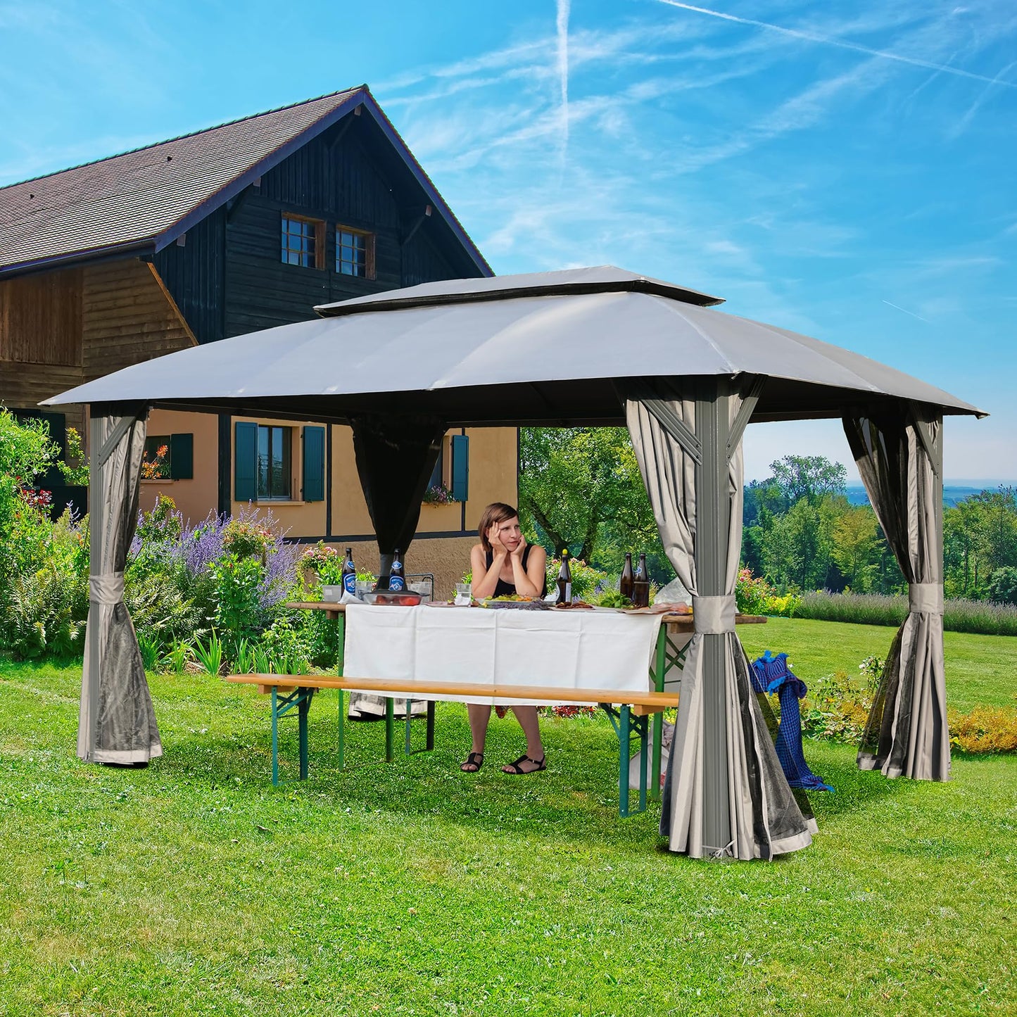 A woman sits at a picnic table under a grey outdoor gazebo with draped curtains set for a gathering
