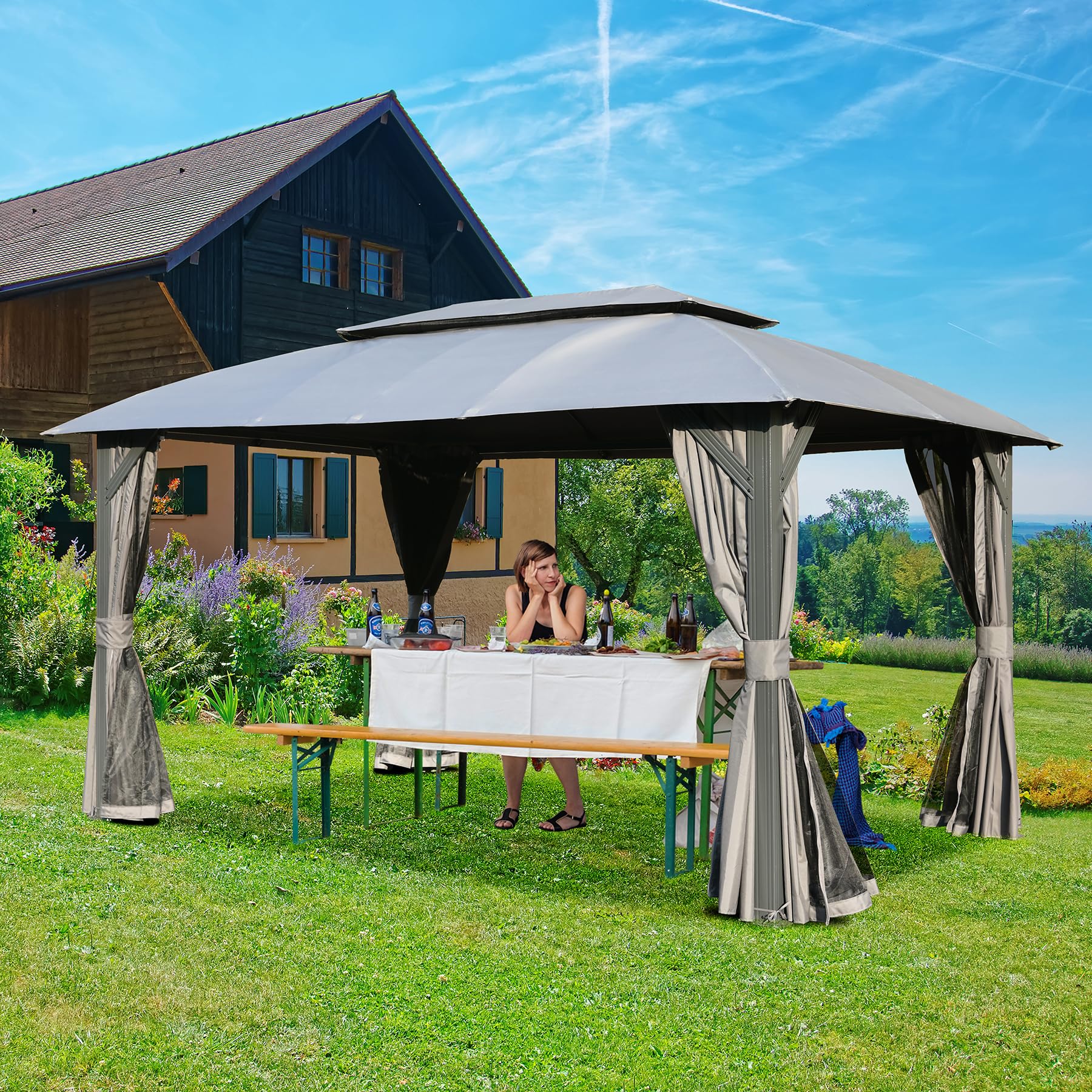 A woman sits at a picnic table under a grey outdoor gazebo with draped curtains set for a gathering