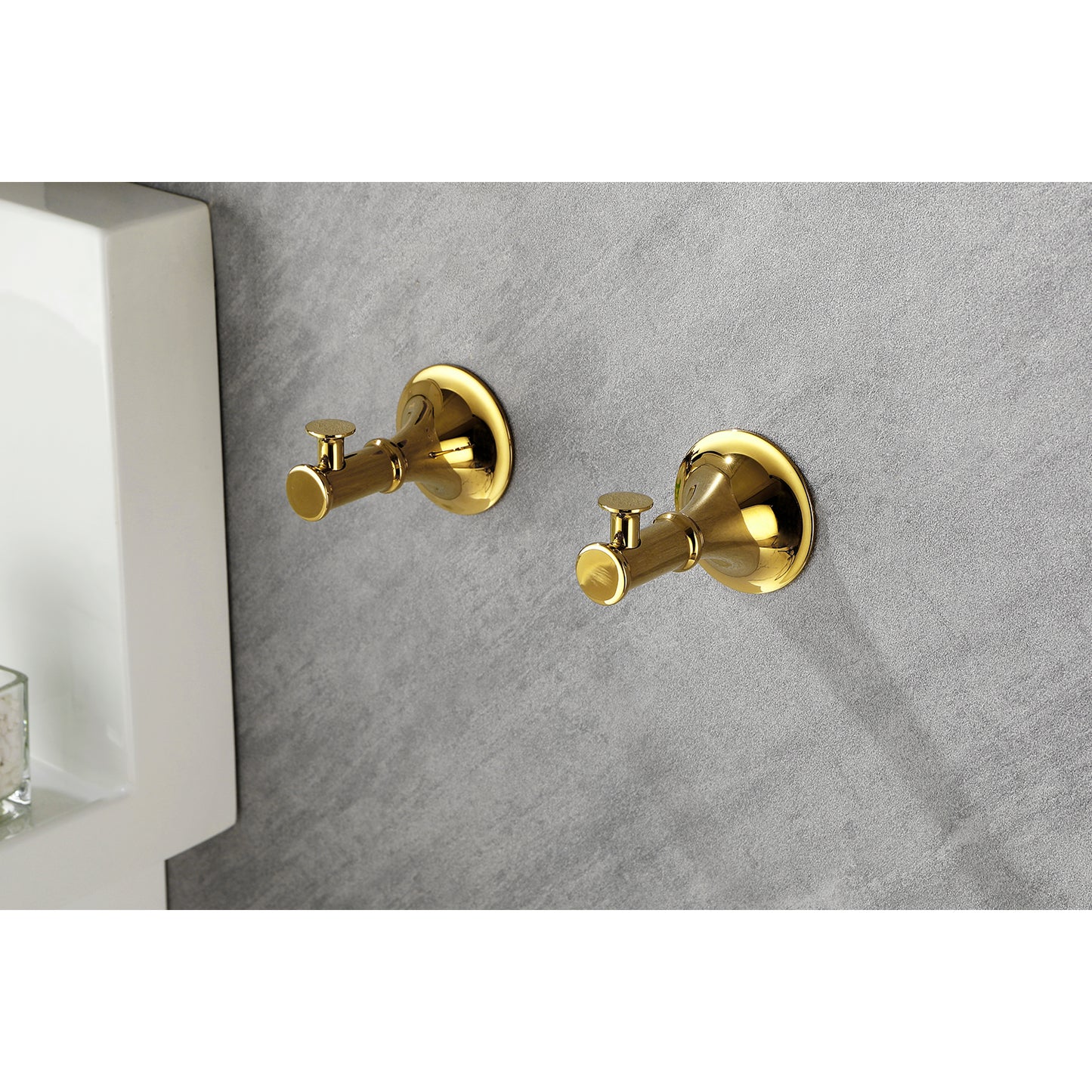 Two polished brass robe hooks mounted on a grey textured wall