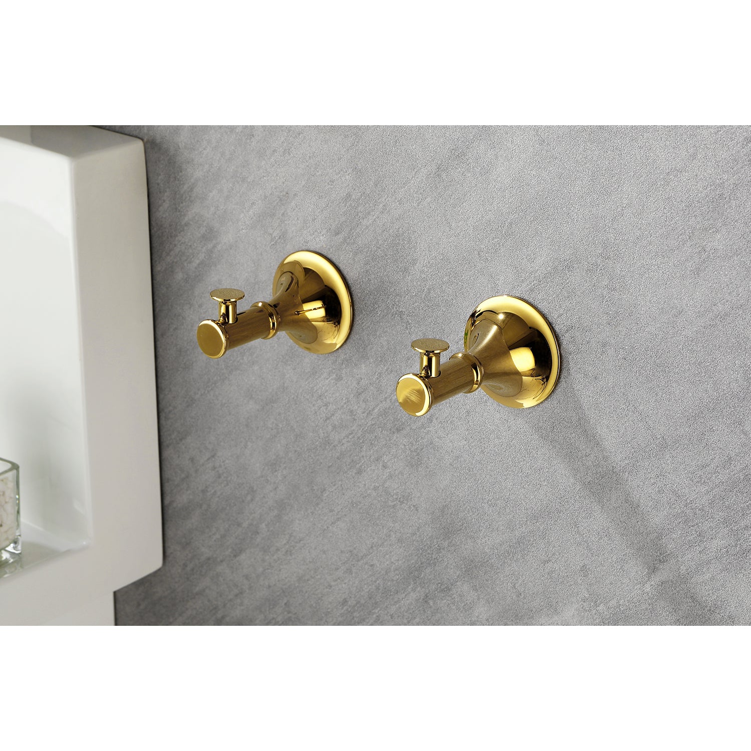 Two polished brass robe hooks mounted on a grey textured wall