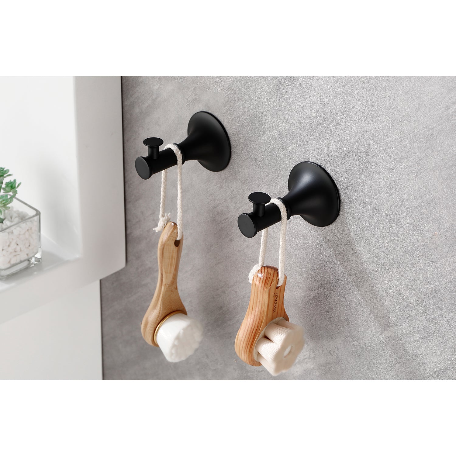 Two black bathroom hooks holding wooden face cleansing brushes with white bristles