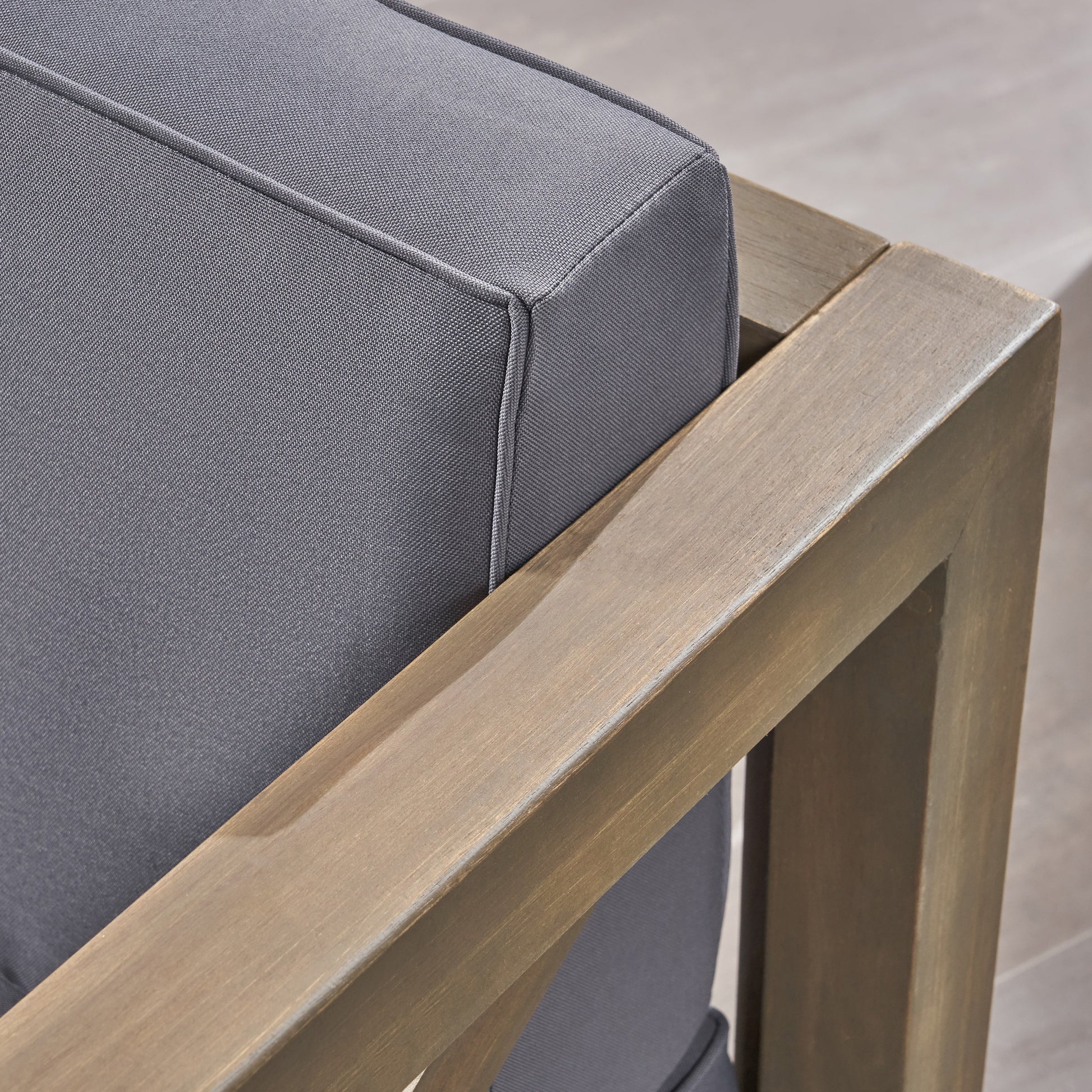 Closeup of a grey outdoor armchair cushion with a wooden frame detail