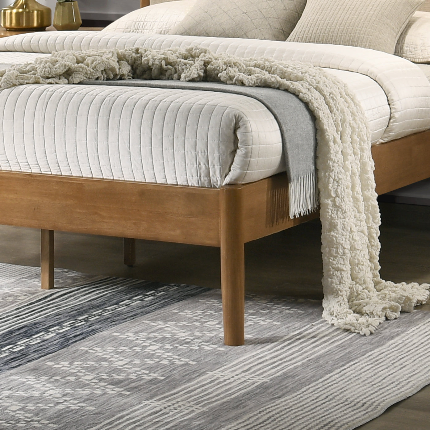 Wooden platform bed frame with a white quilted duvet and cream throw blanket