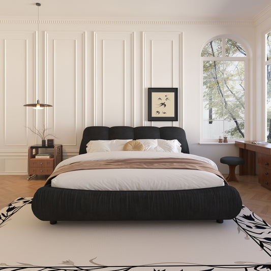 Black upholstered platform bed with white linens and a tan throw