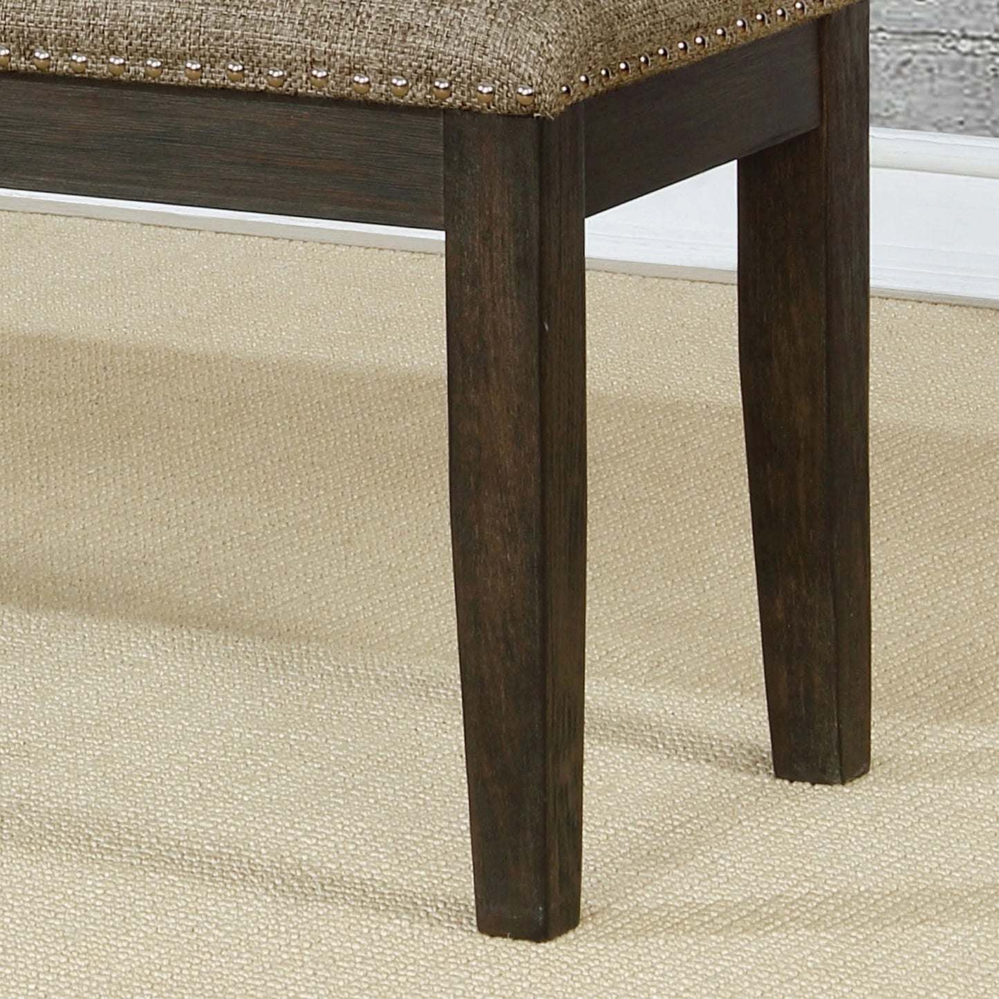 Dark brown wooden legs with nailhead trim on upholstered beige bench