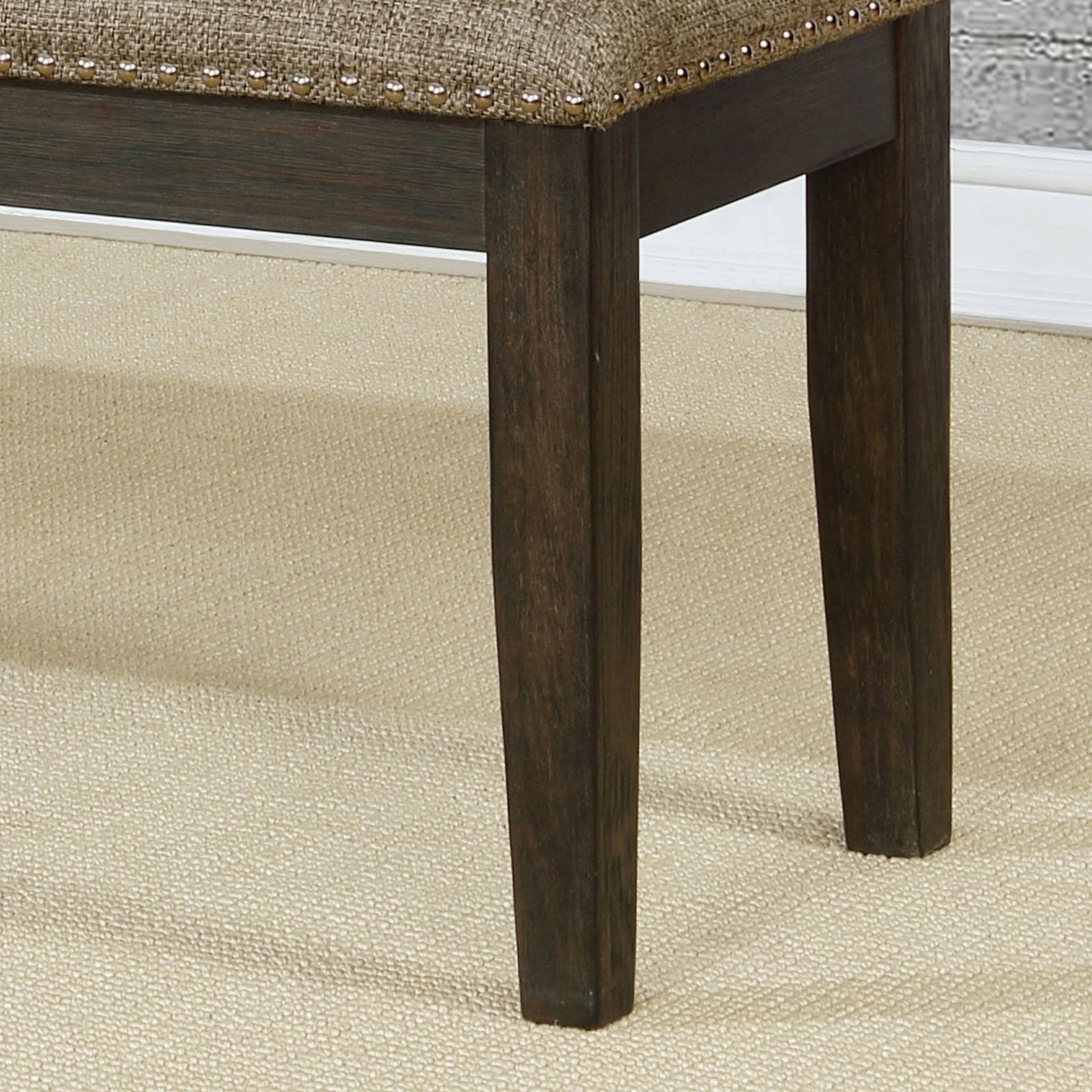 Dark brown wooden legs with nailhead trim on upholstered beige bench