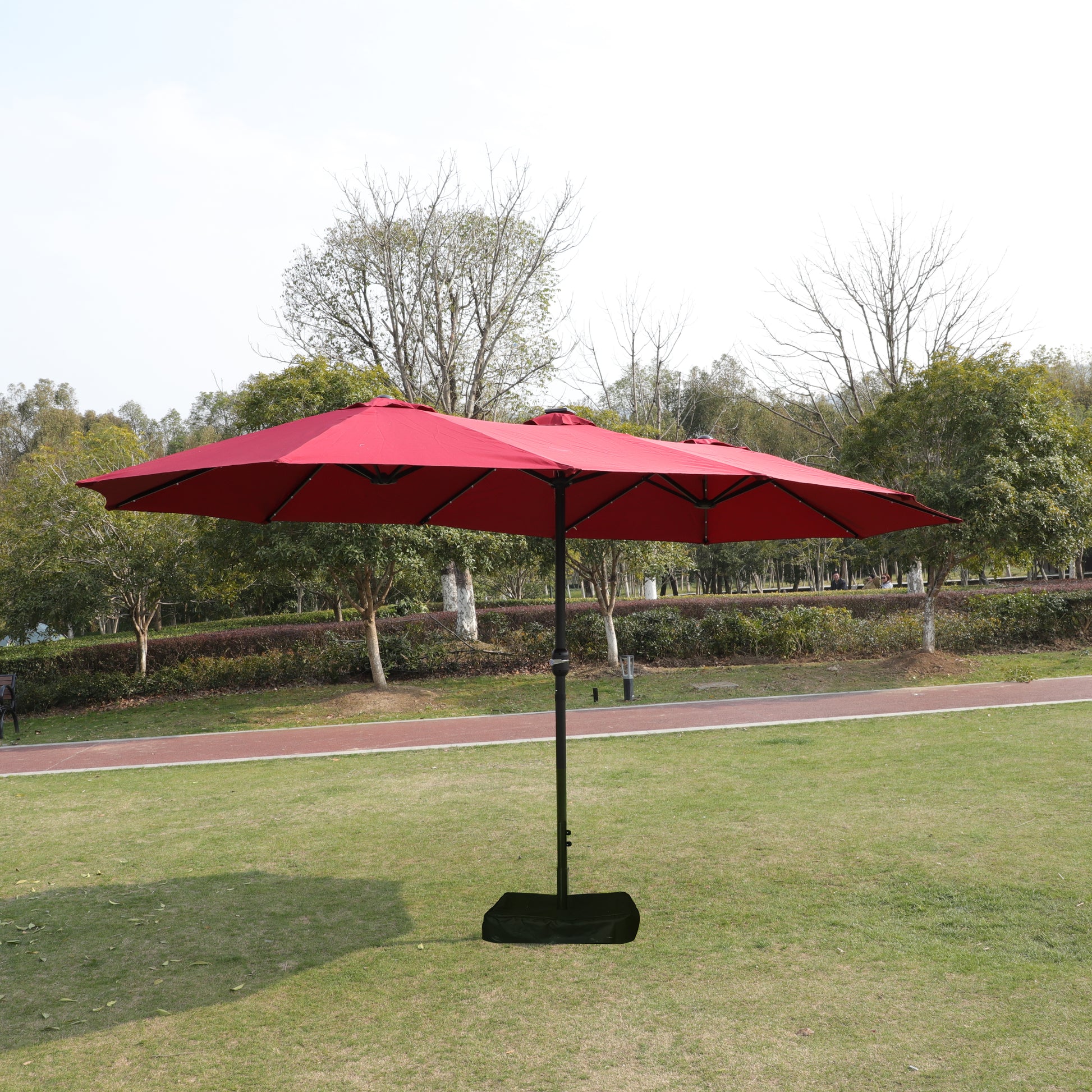 Red double patio umbrella with a black base on a green lawn