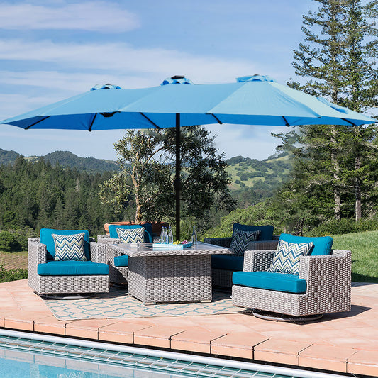 Light gray wicker outdoor furniture set with teal cushions under a large blue umbrella