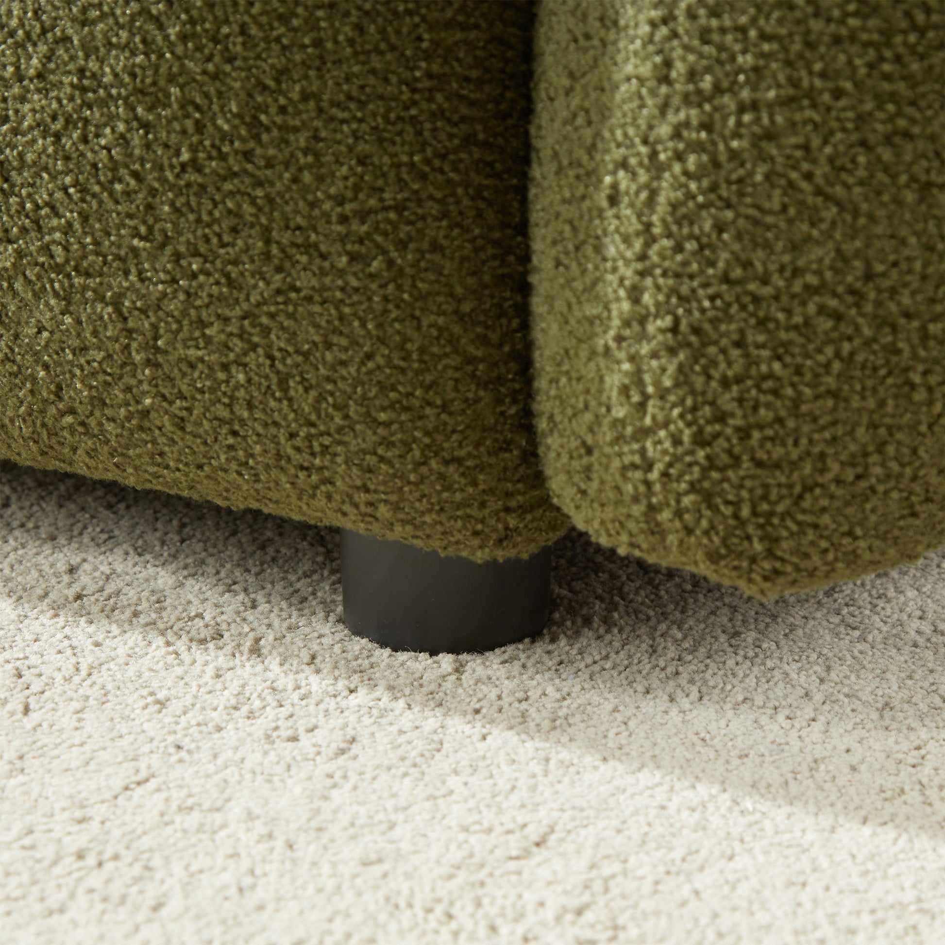 Closeup of textured green sofa fabric with a dark cylindrical leg on a cream rug