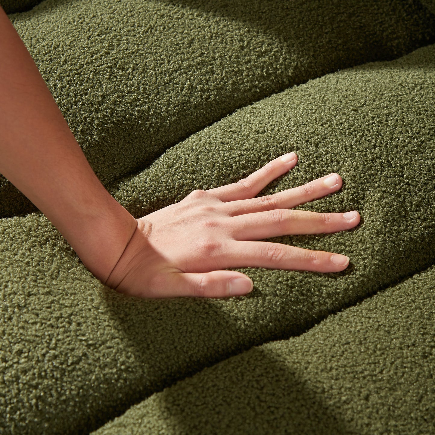 Closeup of a hand pressing into a soft green textured fabric highlighting plush upholstery