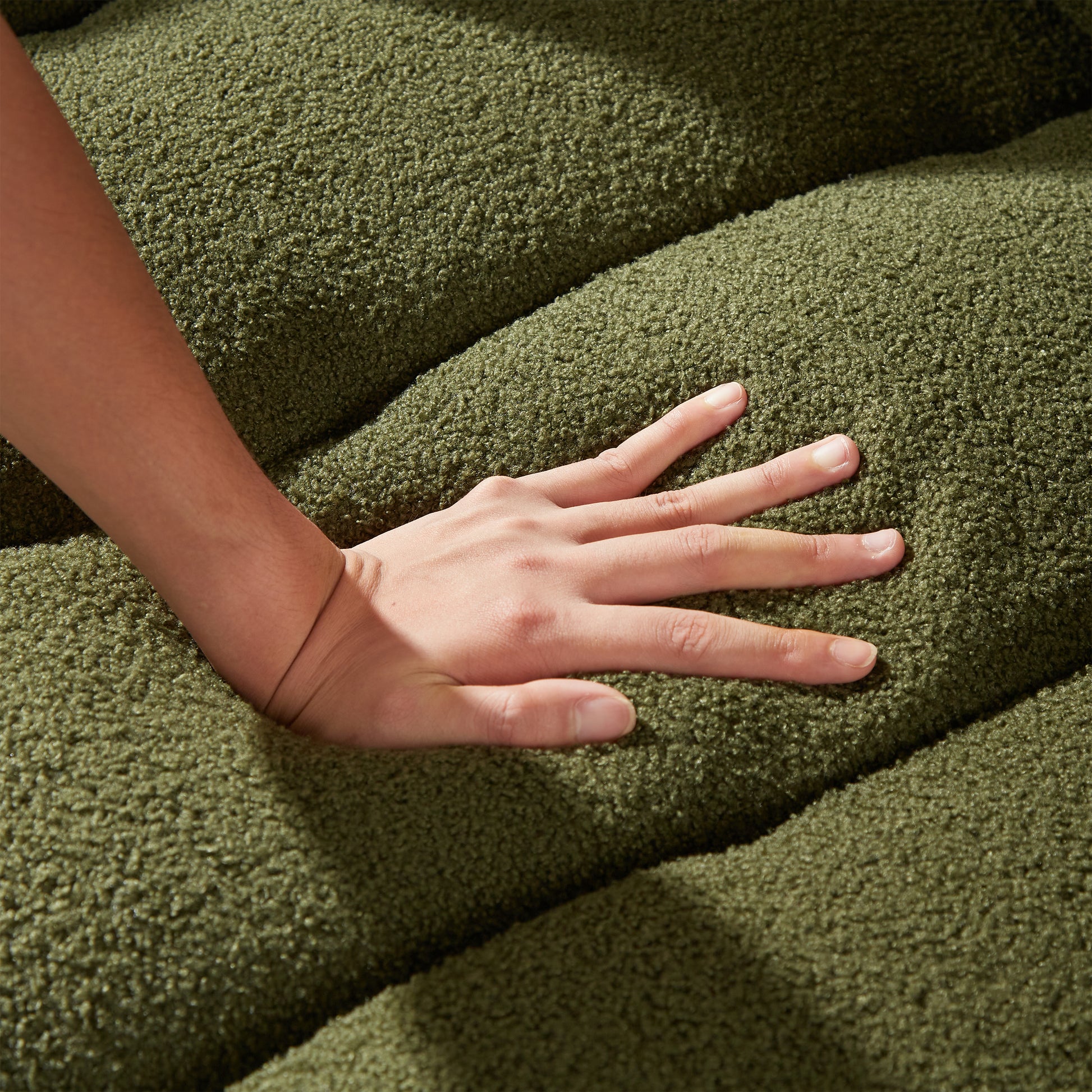 Closeup of a hand pressing into a soft green textured fabric highlighting plush upholstery