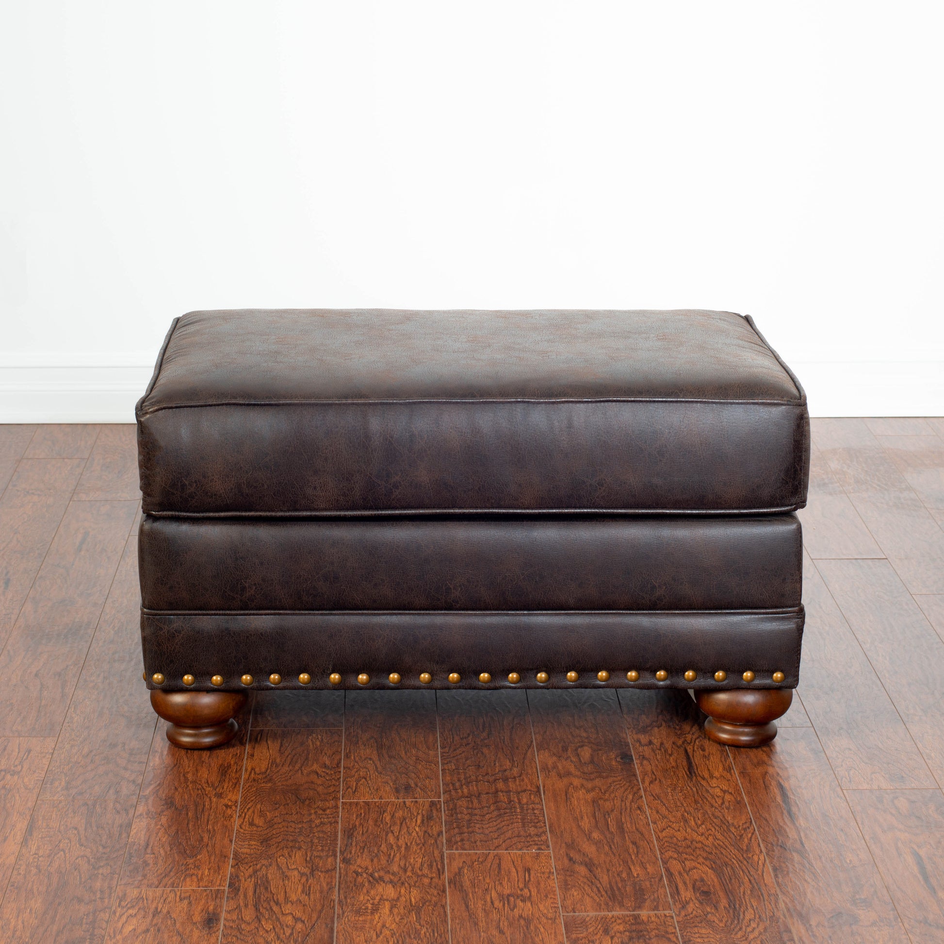 Dark brown faux leather ottoman with antique brass nailhead trim and turned wood feet