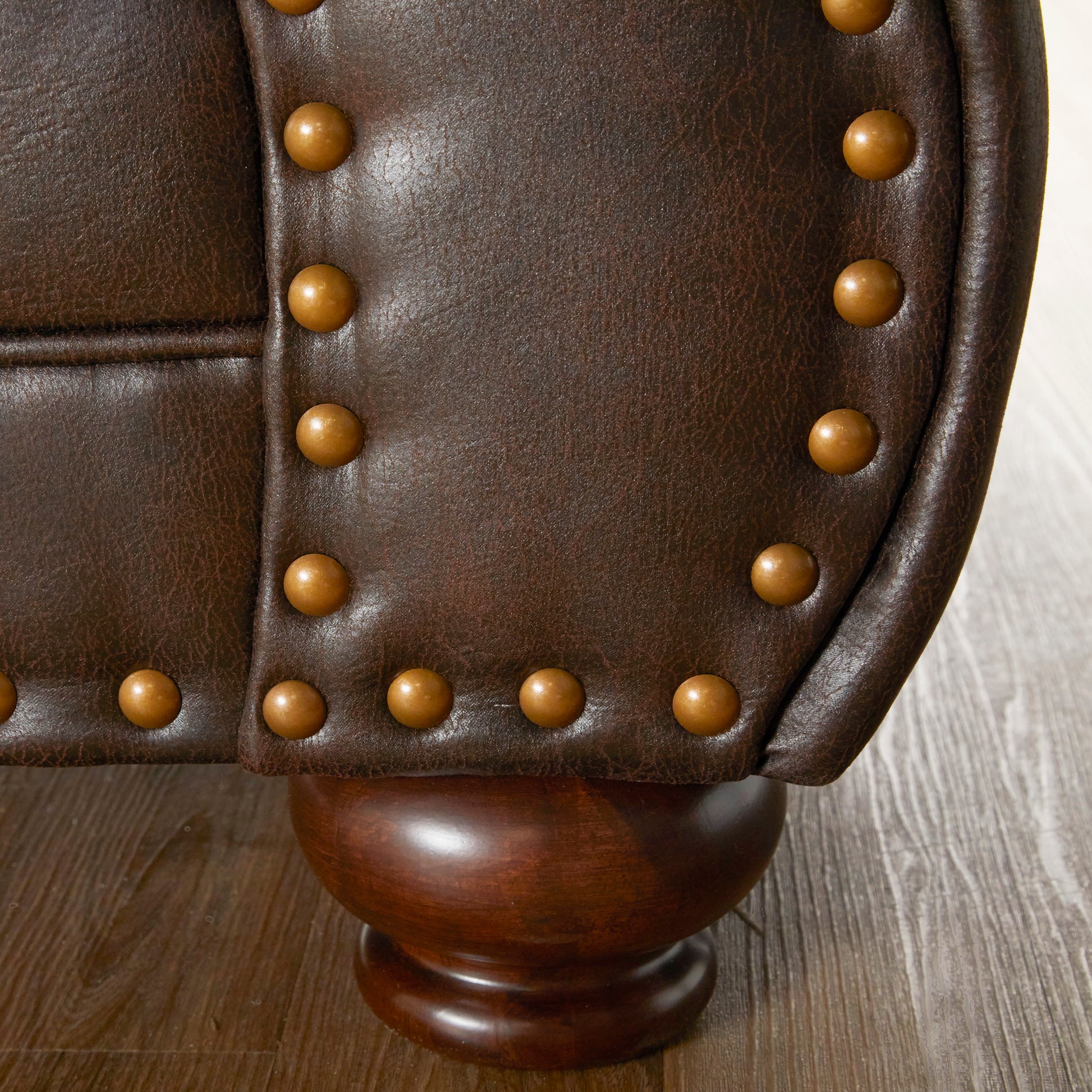 Dark brown tufted leather armchair detail with brass nailhead trim and wooden cabriole leg