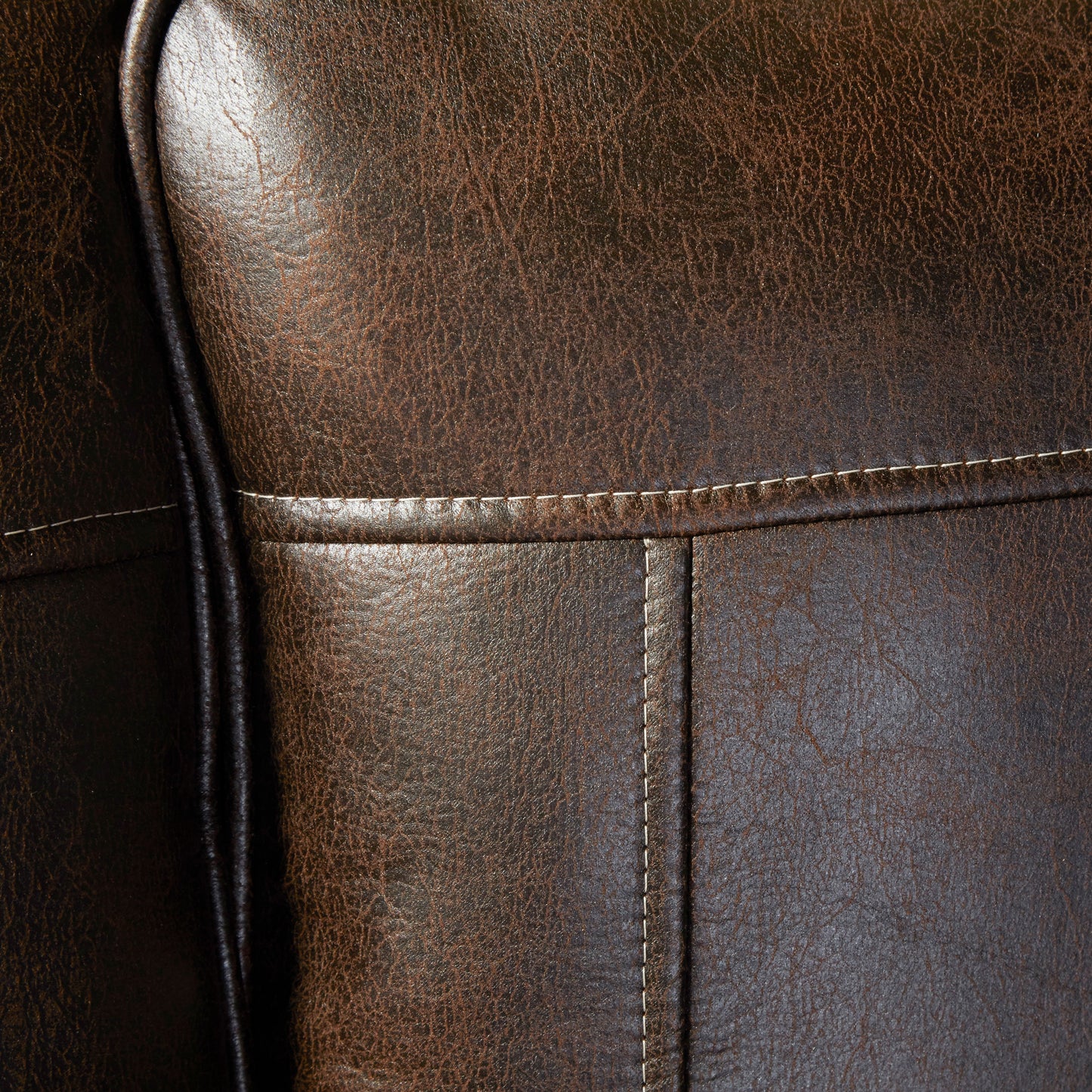 Closeup of rich brown distressed leather upholstery with cream stitching detail