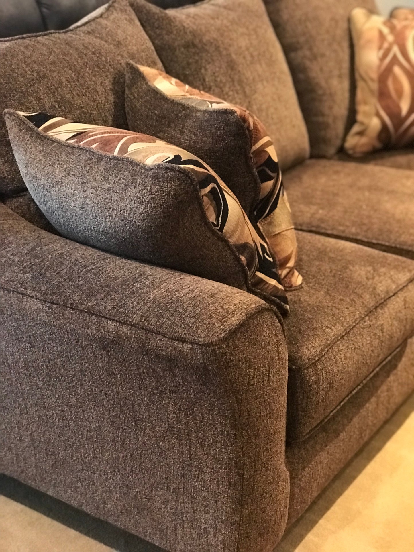 Plush brown sectional sofa with textured fabric and abstract patterned throw pillows