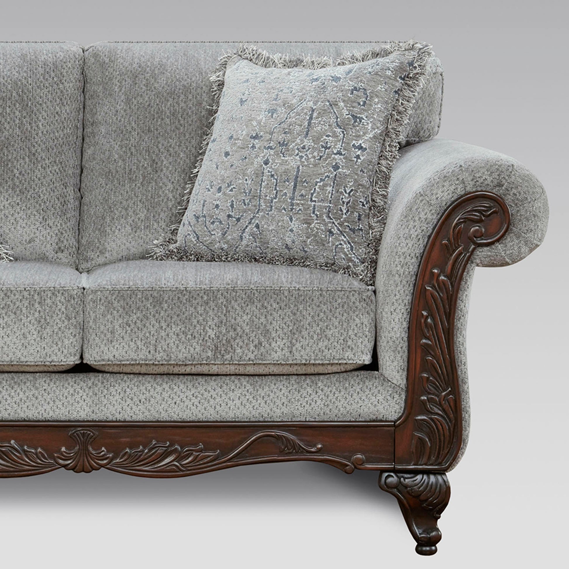 Classic grey upholstered sofa with ornate carved wood armrests and decorative pillow