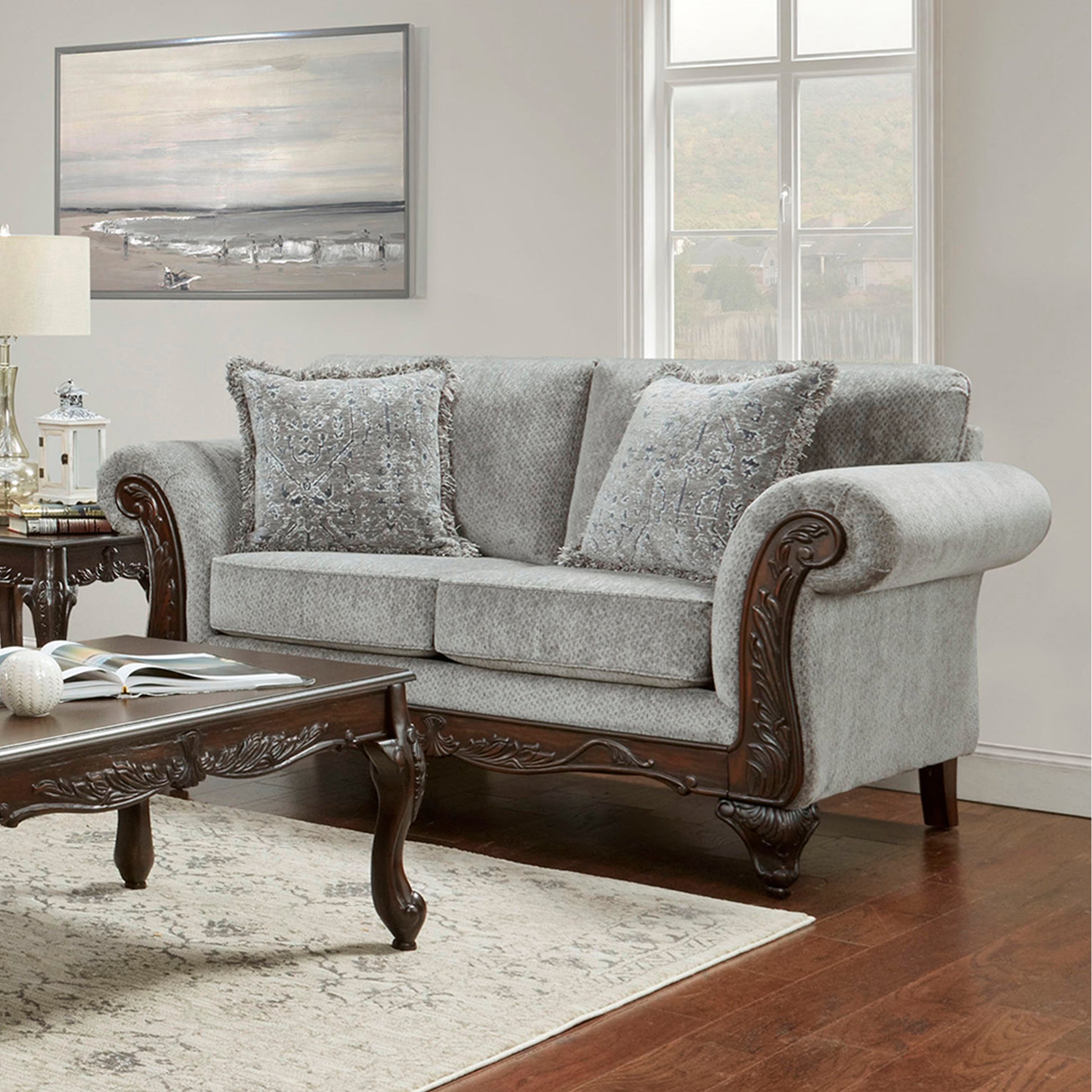 Elegant grey fabric loveseat with ornate carved wooden arms and decorative pillows