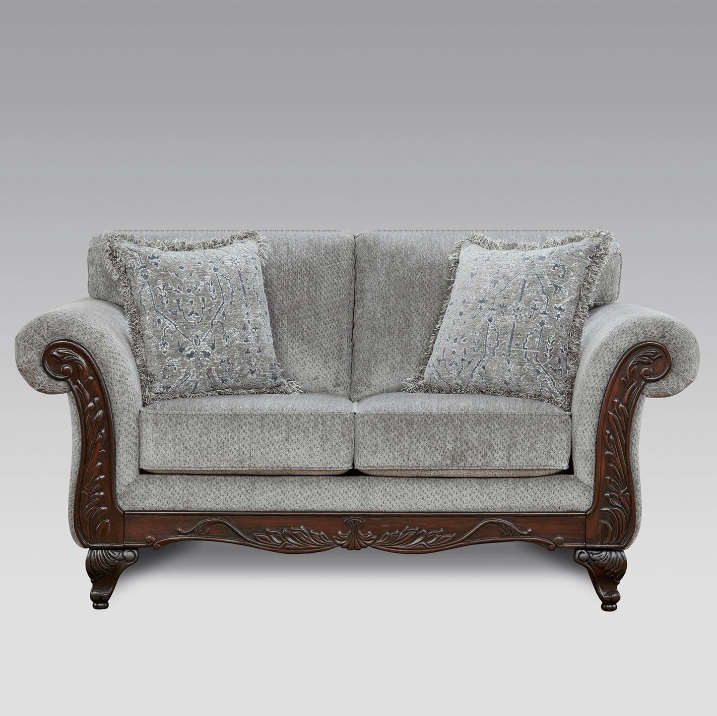Grey fabric loveseat with carved dark wood accents and patterned throw pillows