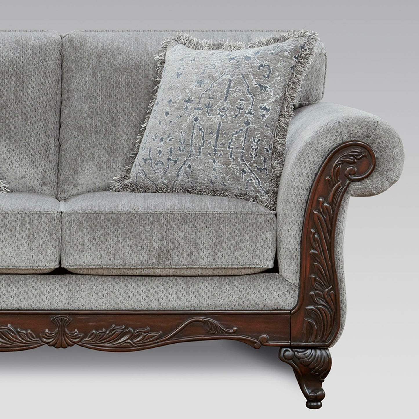 Elegant grey upholstered sofa with ornate carved dark wood armrest and decorative pillow