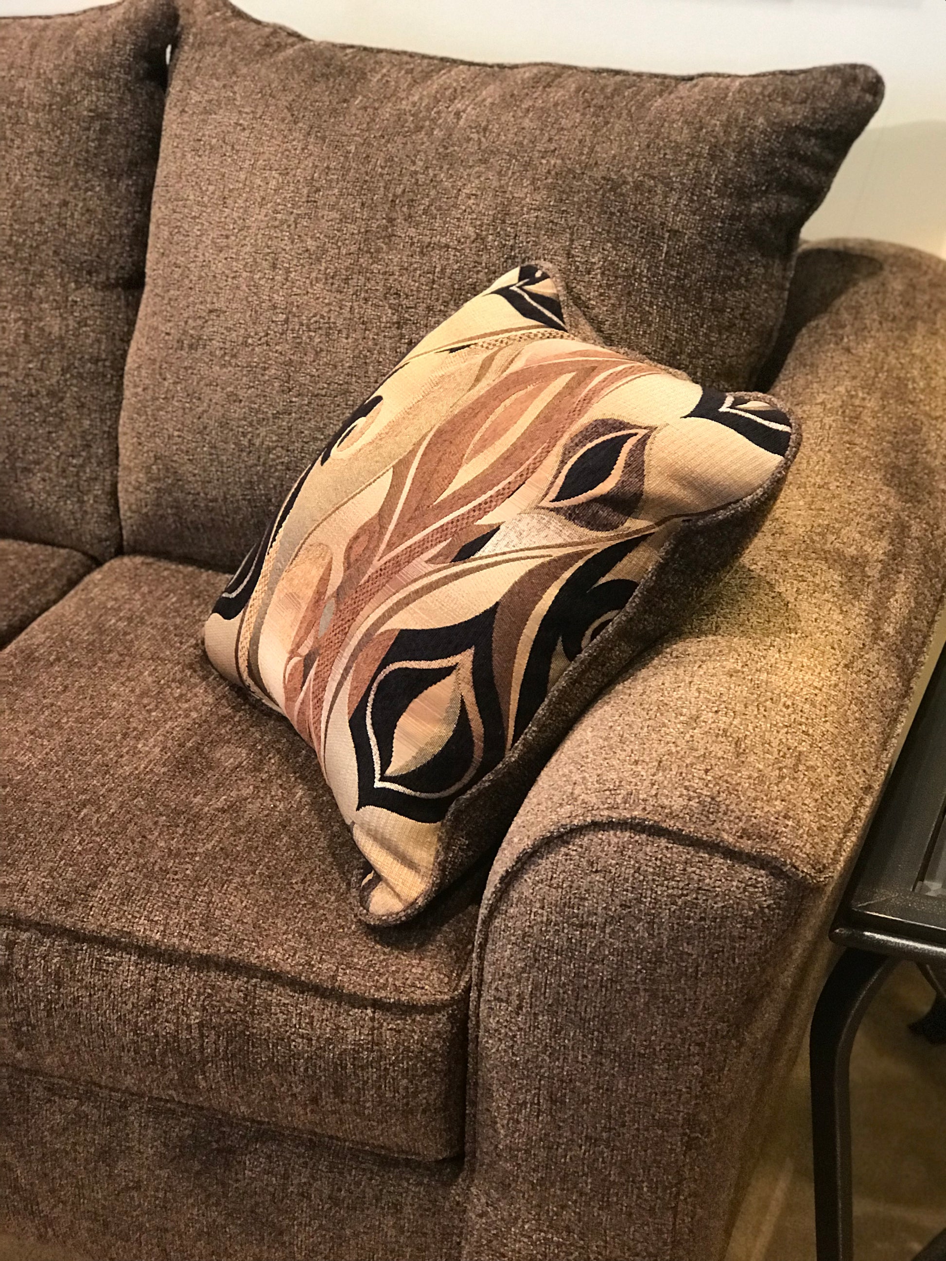 Brown textured throw pillow with abstract brown beige and black leaf pattern on a brown sofa