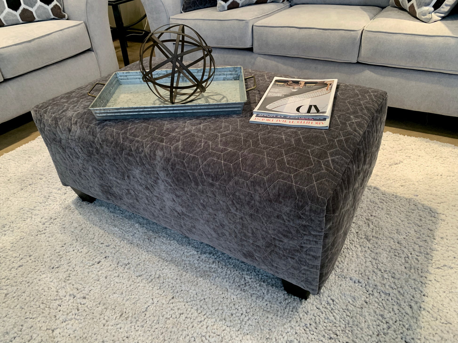 Dark gray upholstered ottoman with hexagonal quilting and a metal decorative sphere