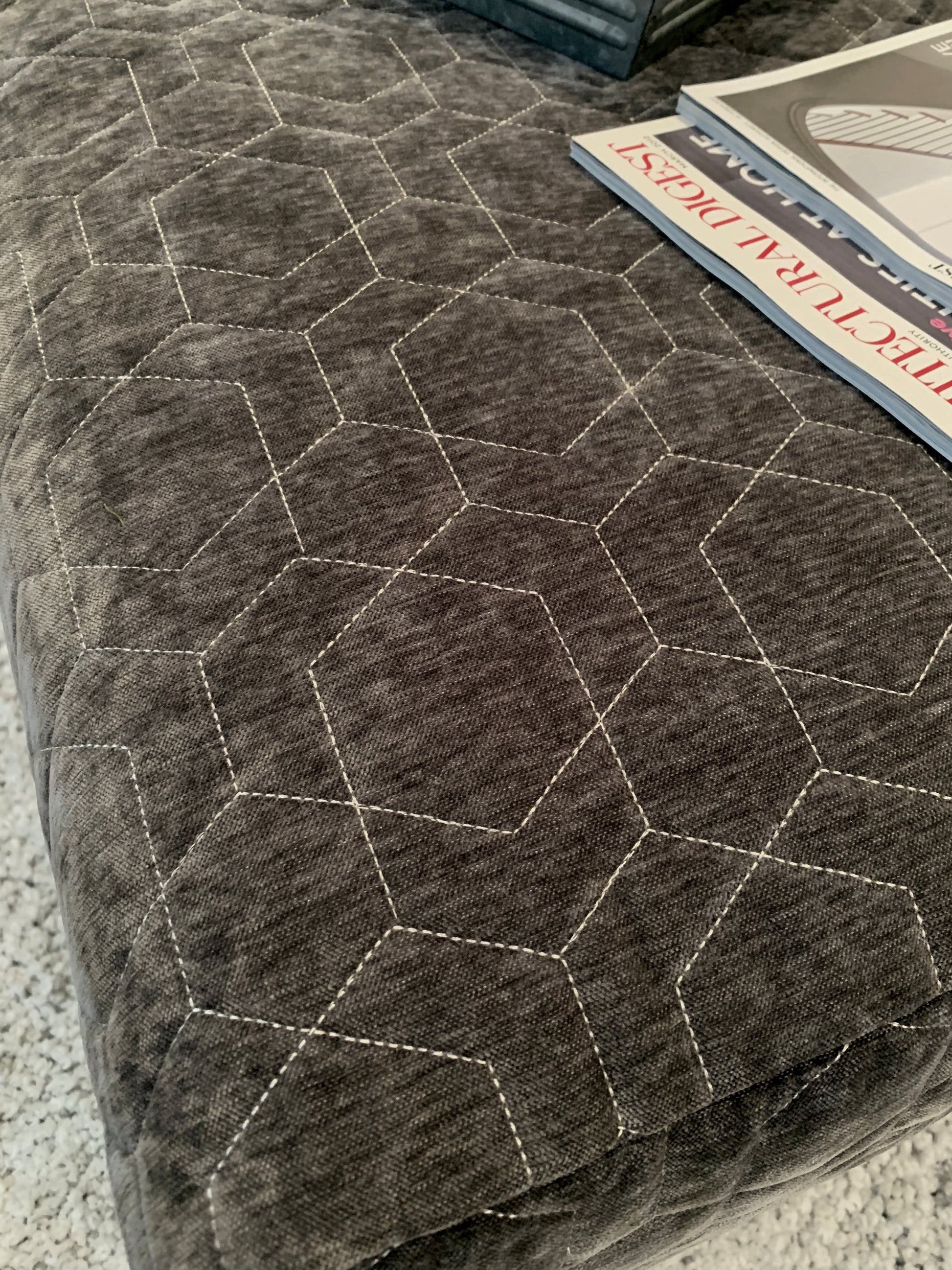Dark gray ottoman upholstered with fabric featuring a whitestitched hexagonal geometric pattern